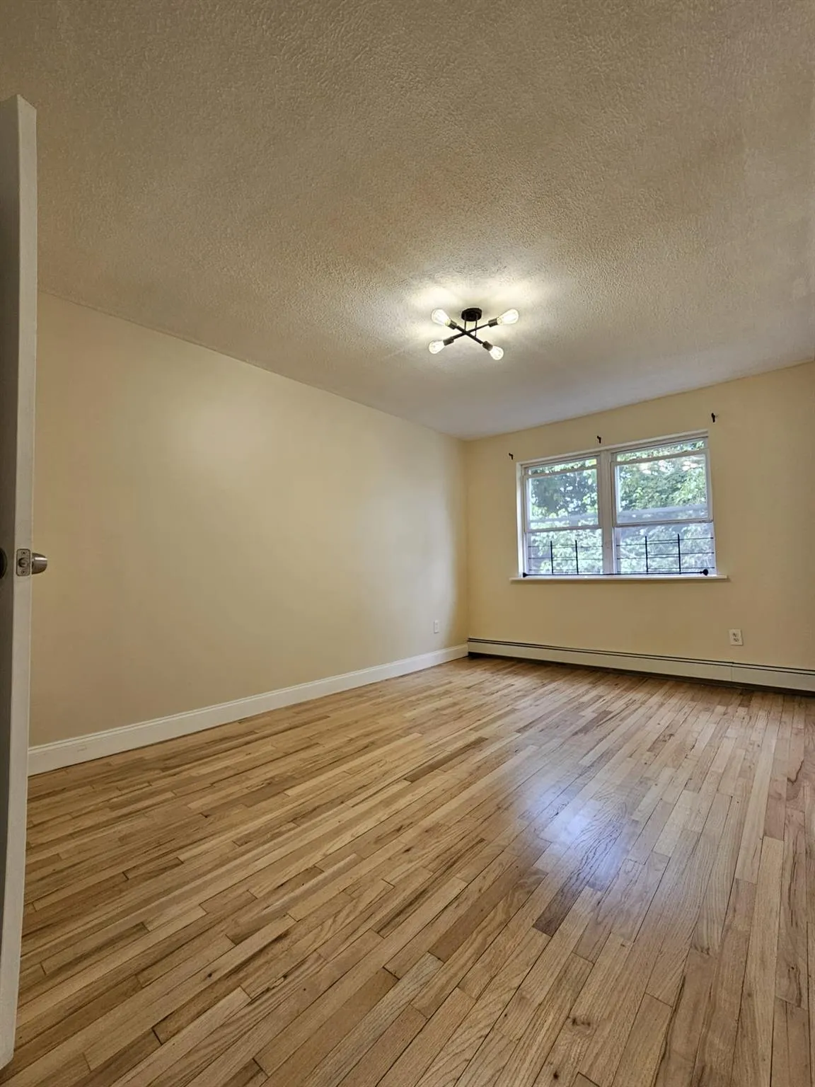 Empty room featuring light wood-style flooring, a baseboard radiator, and a textured ceiling Empty room featuring light wood-style flooring, a baseboard radiator, and a textured ceiling