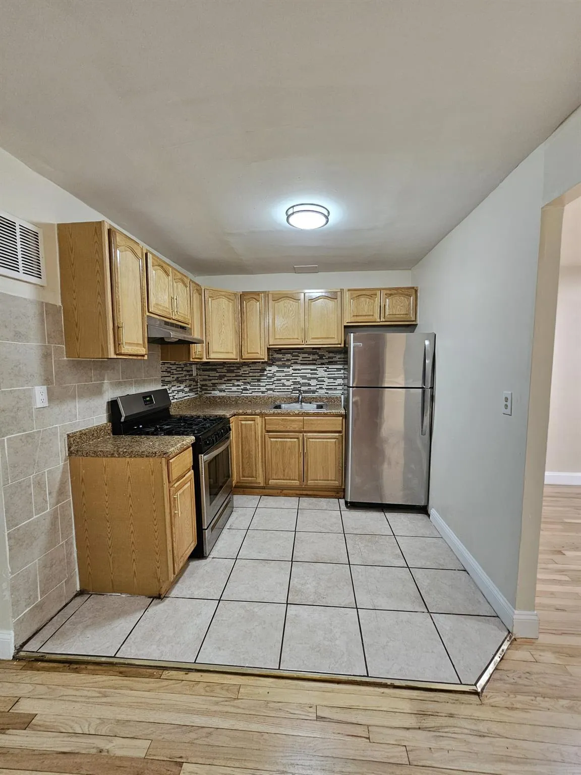 Kitchen featuring appliances with stainless steel finishes, under cabinet range hood, light wood-style flooring, and decorative backsplash Kitchen featuring appliances with stainless steel finishes, under cabinet range hood, light wood-style flooring, and decorative backsplash