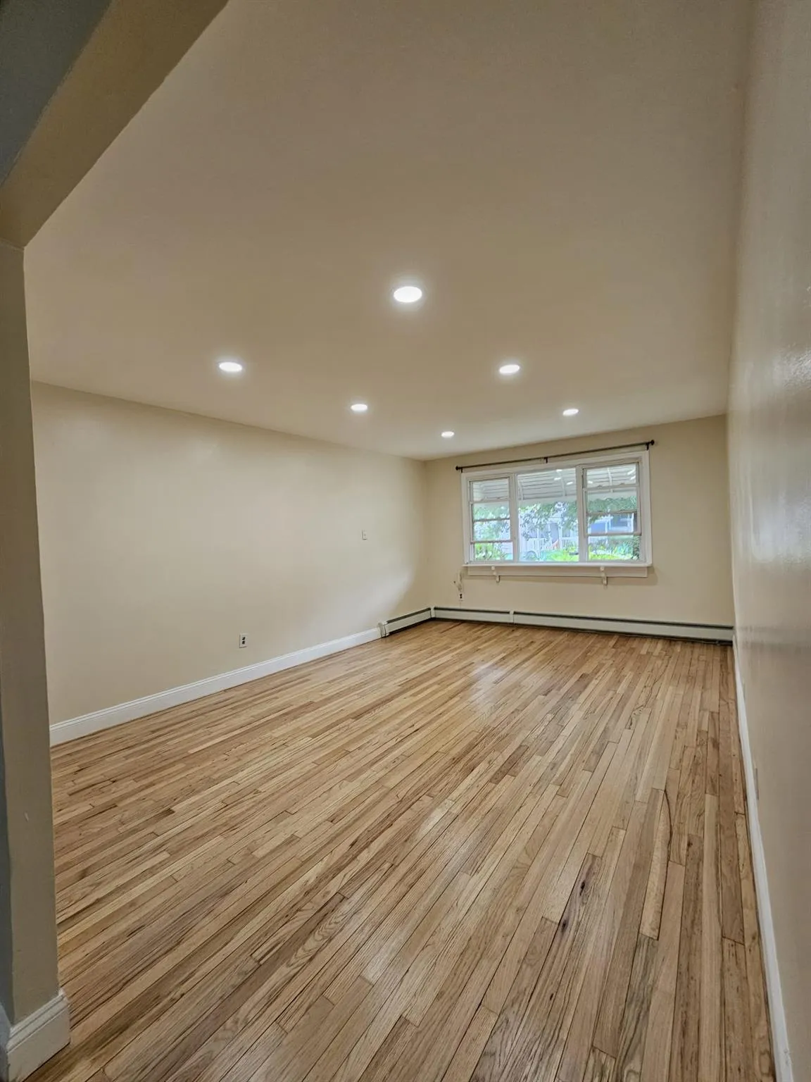 Empty room featuring light wood-type flooring, recessed lighting, and a baseboard heating unit Empty room featuring light wood-type flooring, recessed lighting, and a baseboard heating unit