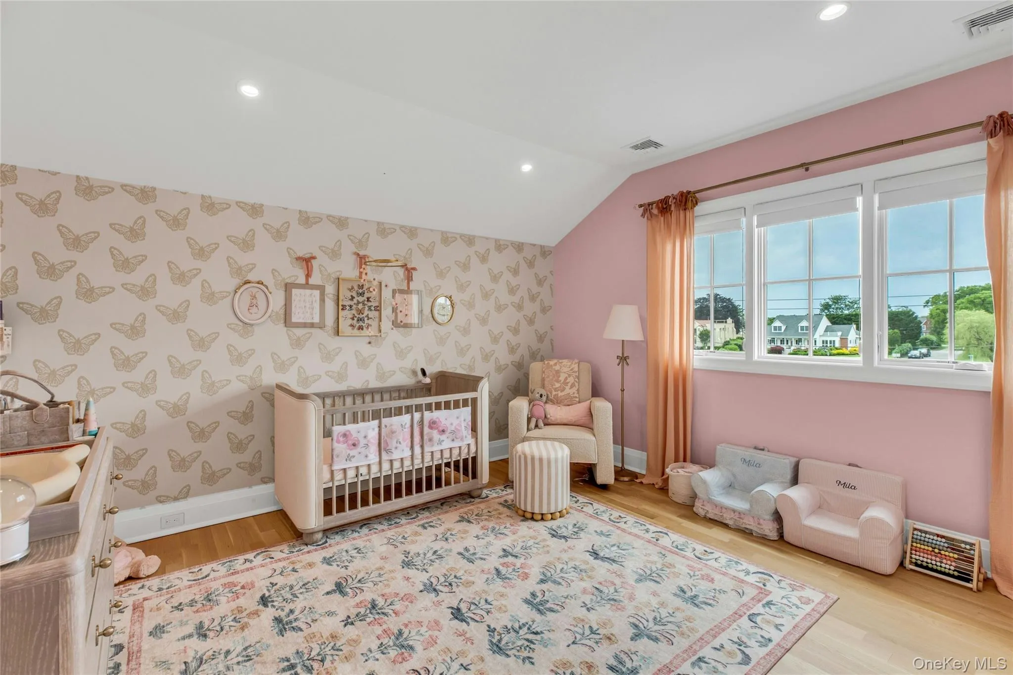Bedroom with wallpapered walls, wood finished floors, lofted ceiling, a crib, and recessed lighting Bedroom with wallpapered walls, wood finished floors, lofted ceiling, a crib, and recessed lighting