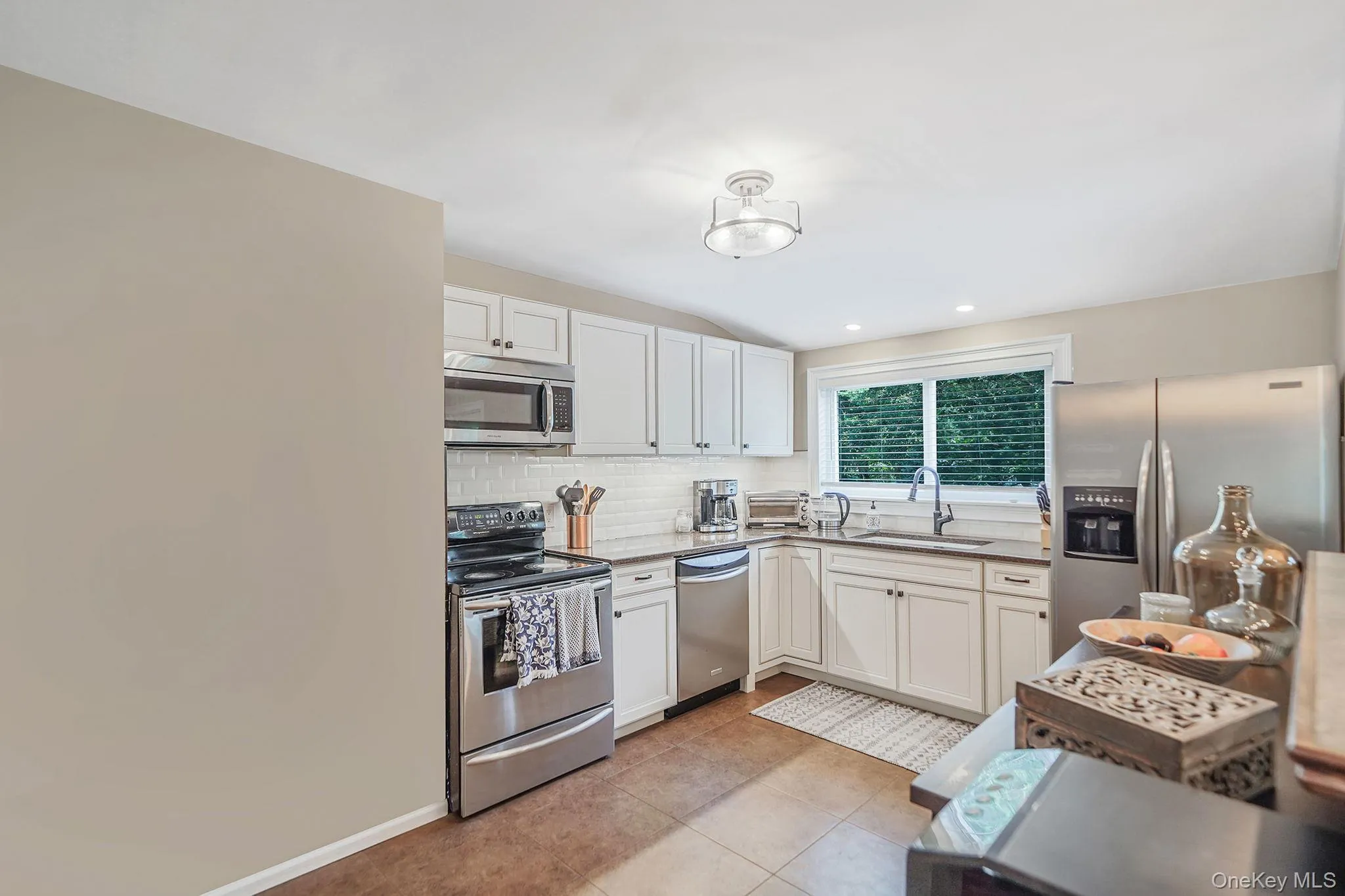 Kitchen featuring appliances with stainless steel finishes, tasteful backsplash, white cabinets, light tile patterned flooring, and light stone counters Kitchen featuring appliances with stainless steel finishes, tasteful backsplash, white cabinets, light tile patterned flooring, and light stone counters