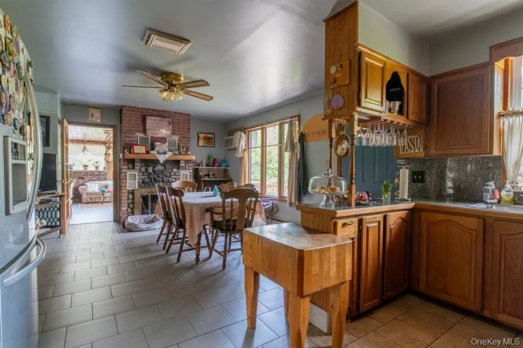 Kitchen with stainless steel fridge with ice dispenser, ceiling fan, tasteful backsplash, a large fireplace, and brown cabinets Kitchen with stainless steel fridge with ice dispenser, ceiling fan, tasteful backsplash, a large fireplace, and brown cabinets