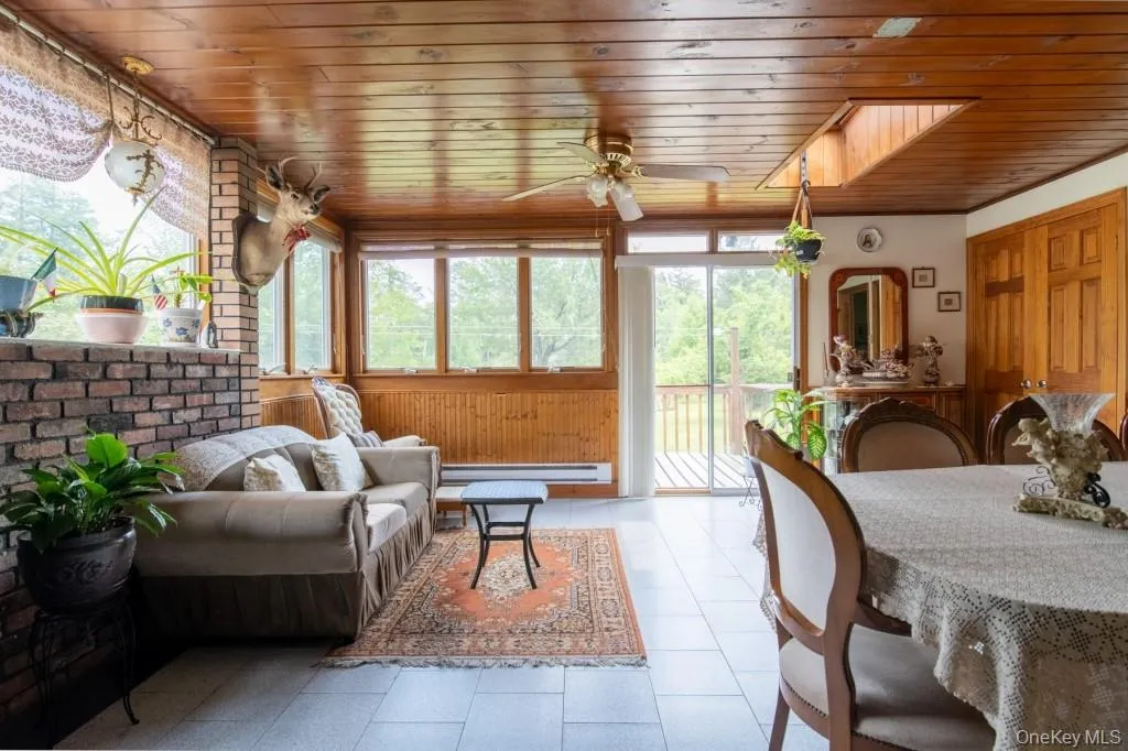 Living room with wooden ceiling, wooden walls, ceiling fan, and a baseboard radiator Living room with wooden ceiling, wooden walls, ceiling fan, and a baseboard radiator