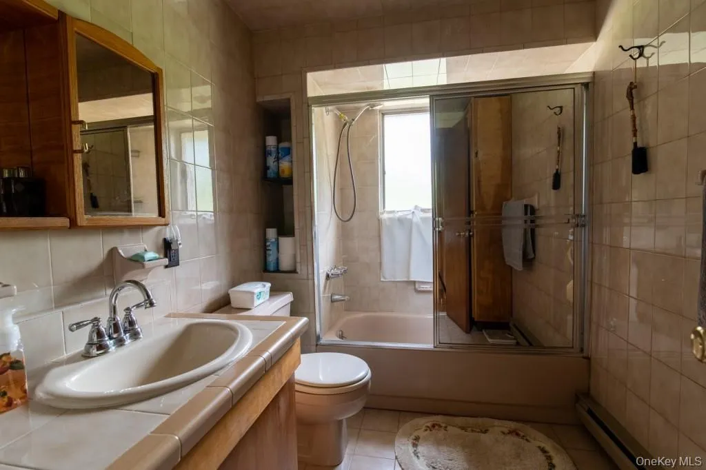 Bathroom with tile walls, a baseboard radiator, vanity, combined bath / shower with glass door, and tile patterned flooring Bathroom with tile walls, a baseboard radiator, vanity, combined bath / shower with glass door, and tile patterned flooring