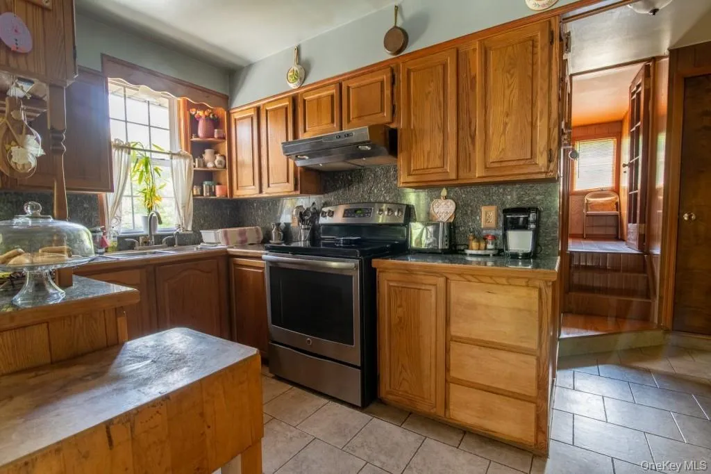 Kitchen featuring stainless steel electric stove, light tile patterned floors, healthy amount of natural light, and under cabinet range hood Kitchen featuring stainless steel electric stove, light tile patterned floors, healthy amount of natural light, and under cabinet range hood