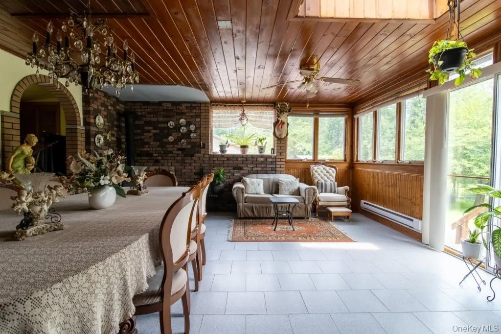 Dining area featuring wood ceiling, a baseboard heating unit, brick wall, a ceiling fan, and wooden walls Dining area featuring wood ceiling, a baseboard heating unit, brick wall, a ceiling fan, and wooden walls