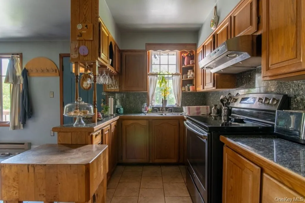 Kitchen with black / electric stove, under cabinet range hood, backsplash, a peninsula, and light tile patterned floors Kitchen with black / electric stove, under cabinet range hood, backsplash, a peninsula, and light tile patterned floors