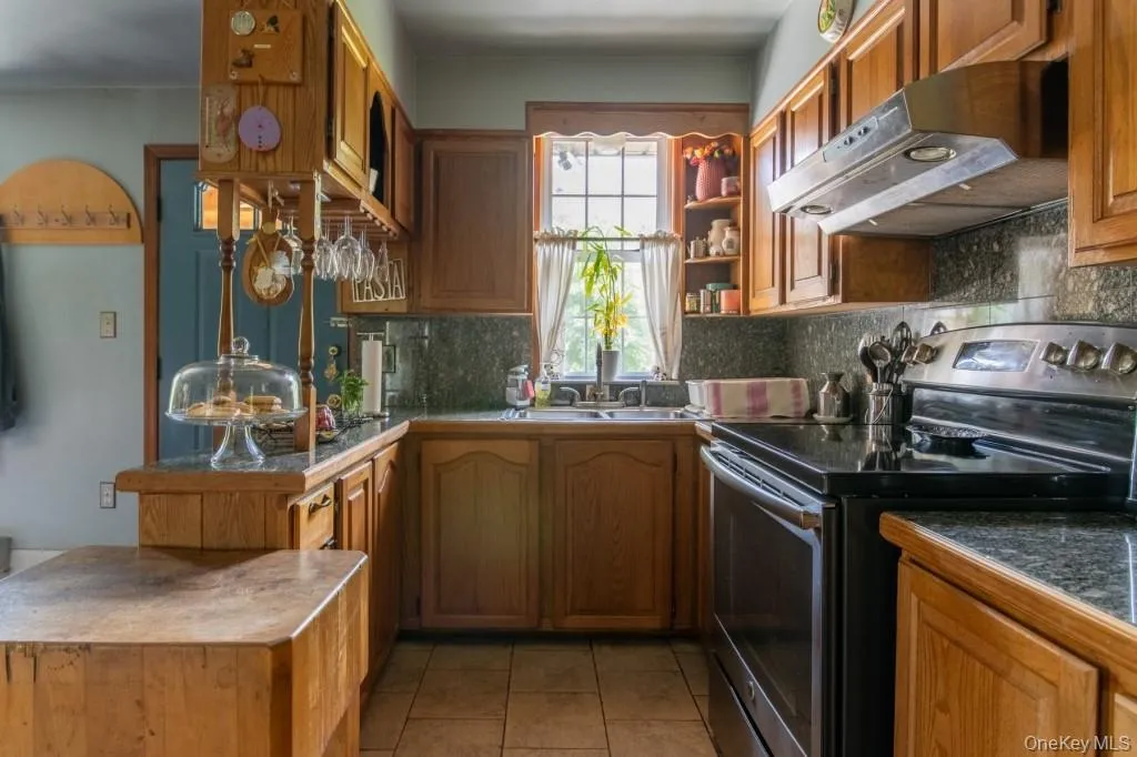 Kitchen with stainless steel range with electric stovetop, under cabinet range hood, light tile patterned flooring, a peninsula, and backsplash Kitchen with stainless steel range with electric stovetop, under cabinet range hood, light tile patterned flooring, a peninsula, and backsplash