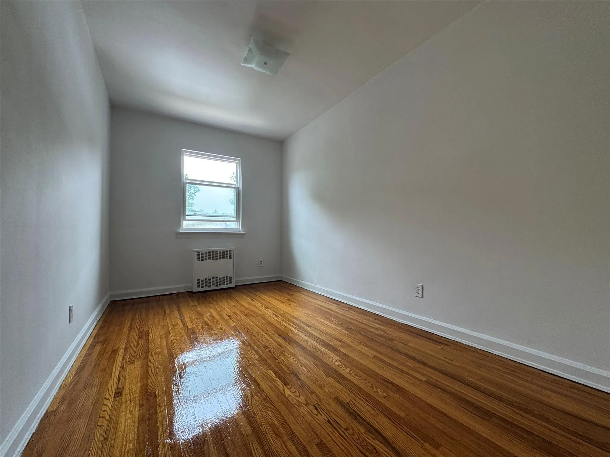 Unfurnished room featuring radiator heating unit and wood finished floors Unfurnished room featuring radiator heating unit and wood finished floors