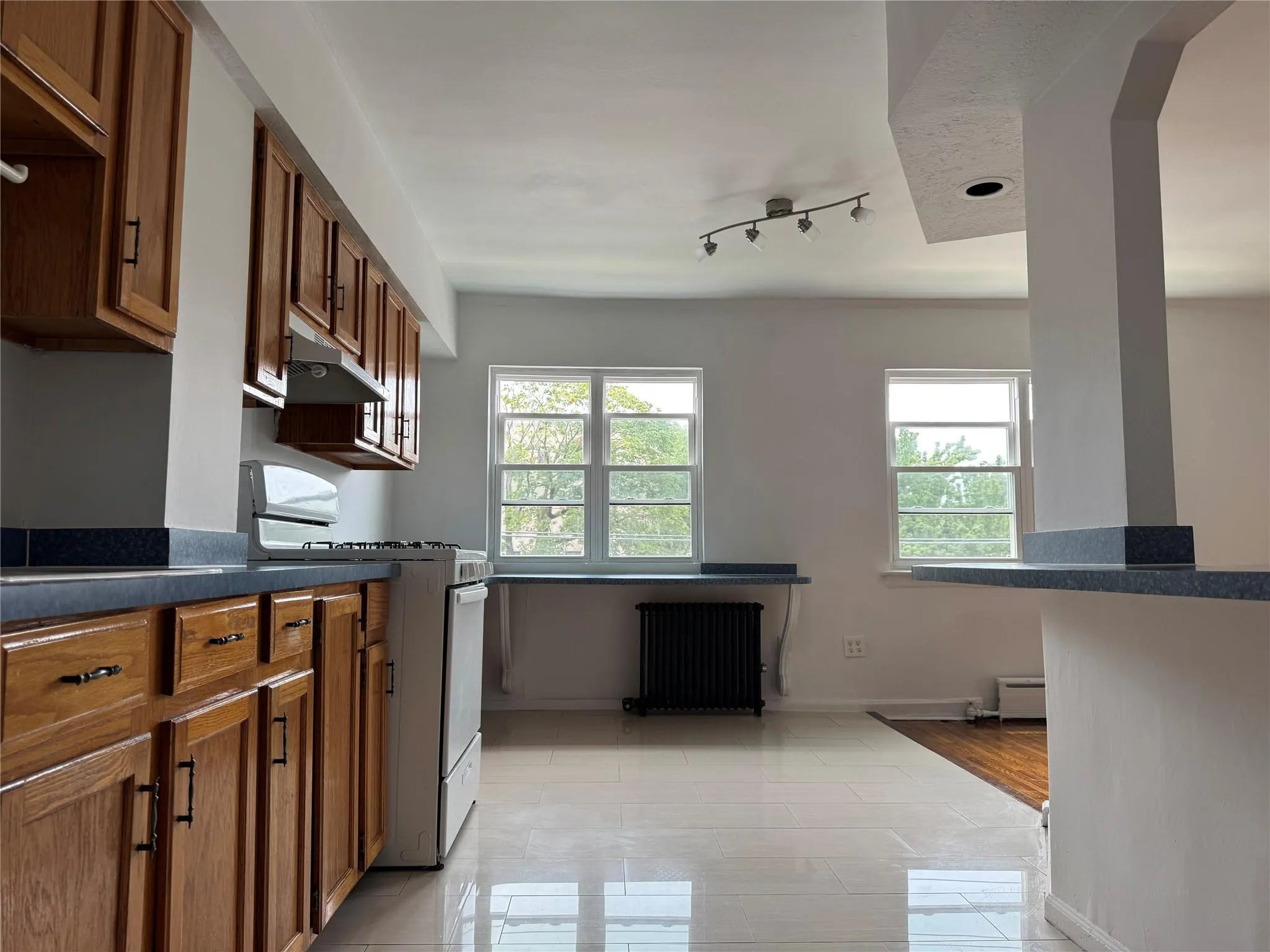 Kitchen featuring radiator, gas range, dark countertops, under cabinet range hood, and rail lighting Kitchen featuring radiator, gas range, dark countertops, under cabinet range hood, and rail lighting