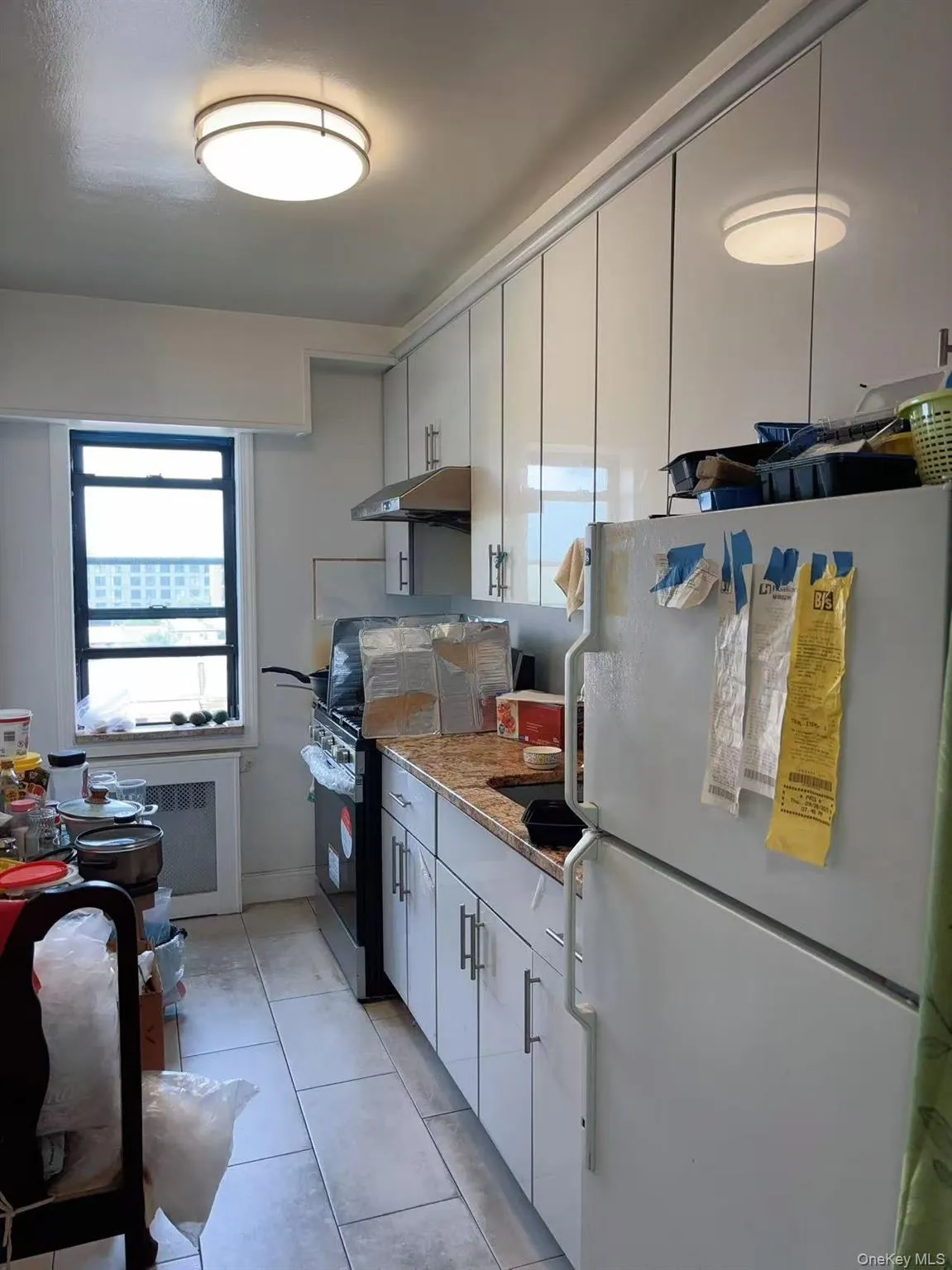 Kitchen with freestanding refrigerator, under cabinet range hood, range with electric cooktop, light tile patterned floors, and white cabinets Kitchen with freestanding refrigerator, under cabinet range hood, range with electric cooktop, light tile patterned floors, and white cabinets