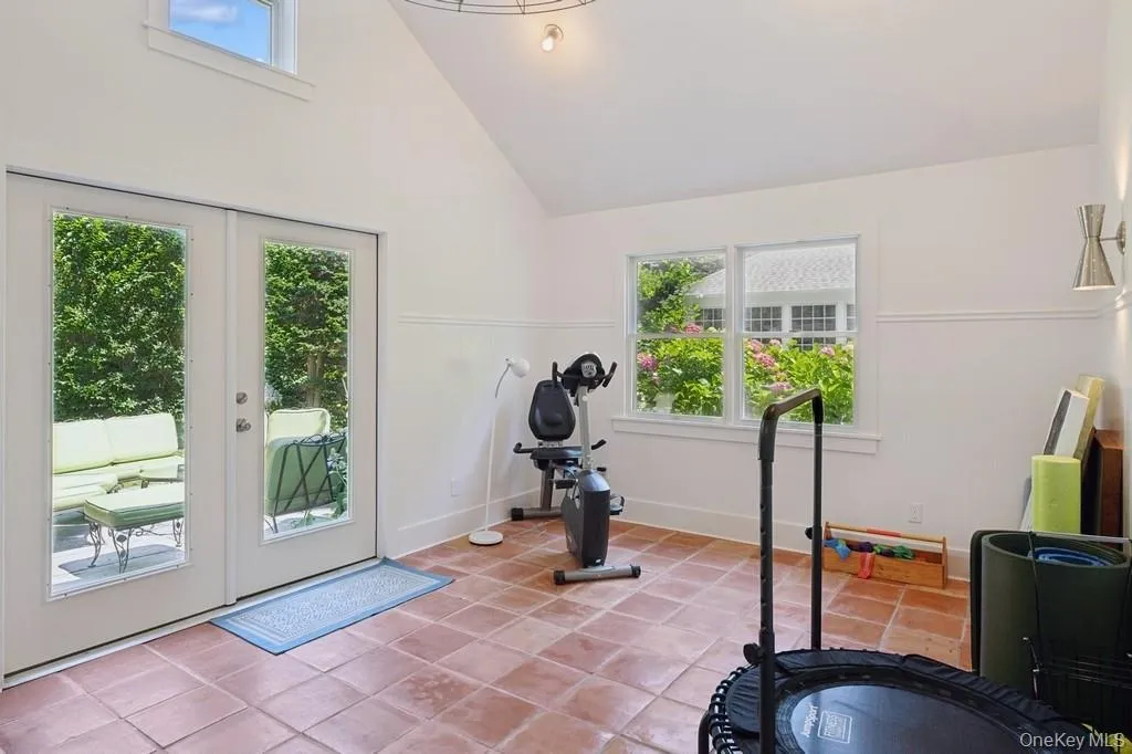 Pool house. Workout area with light tile patterned flooring, high vaulted ceiling, a wainscoted wall, and french doors Pool house. Workout area with light tile patterned flooring, high vaulted ceiling, a wainscoted wall, and french doors