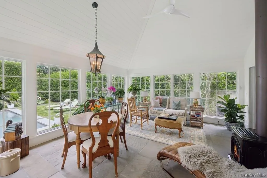 Sunroom / solarium featuring vaulted ceiling, plenty of natural light, a wood stove, and stone tile flooring Sunroom / solarium featuring vaulted ceiling, plenty of natural light, a wood stove, and stone tile flooring