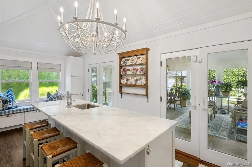 Kitchen with french doors, plenty of natural light, light stone countertops, a center island with sink, and vaulted ceiling Kitchen with french doors, plenty of natural light, light stone countertops, a center island with sink, and vaulted ceiling