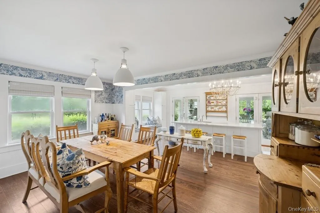 Dining room with wood finished floors, wallpapered walls, crown molding, and a chandelier Dining room with wood finished floors, wallpapered walls, crown molding, and a chandelier