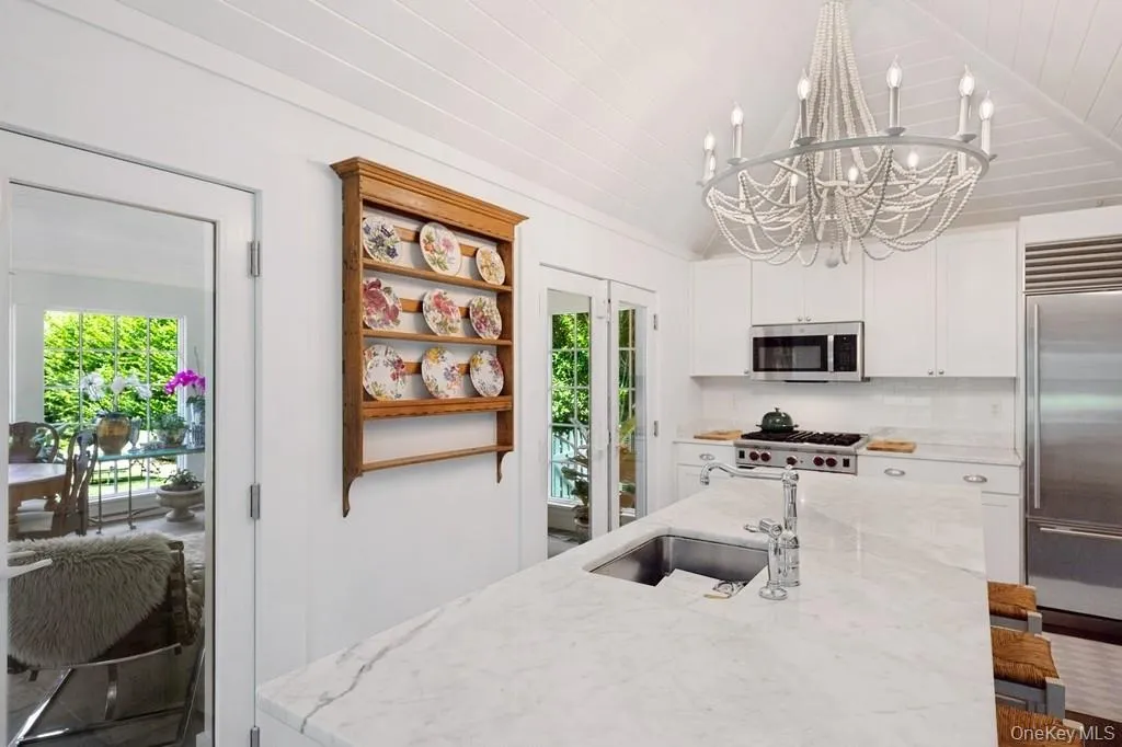 Kitchen featuring stainless steel appliances, a chandelier, healthy amount of natural light, vaulted ceiling, and tasteful backsplash Kitchen featuring stainless steel appliances, a chandelier, healthy amount of natural light, vaulted ceiling, and tasteful backsplash