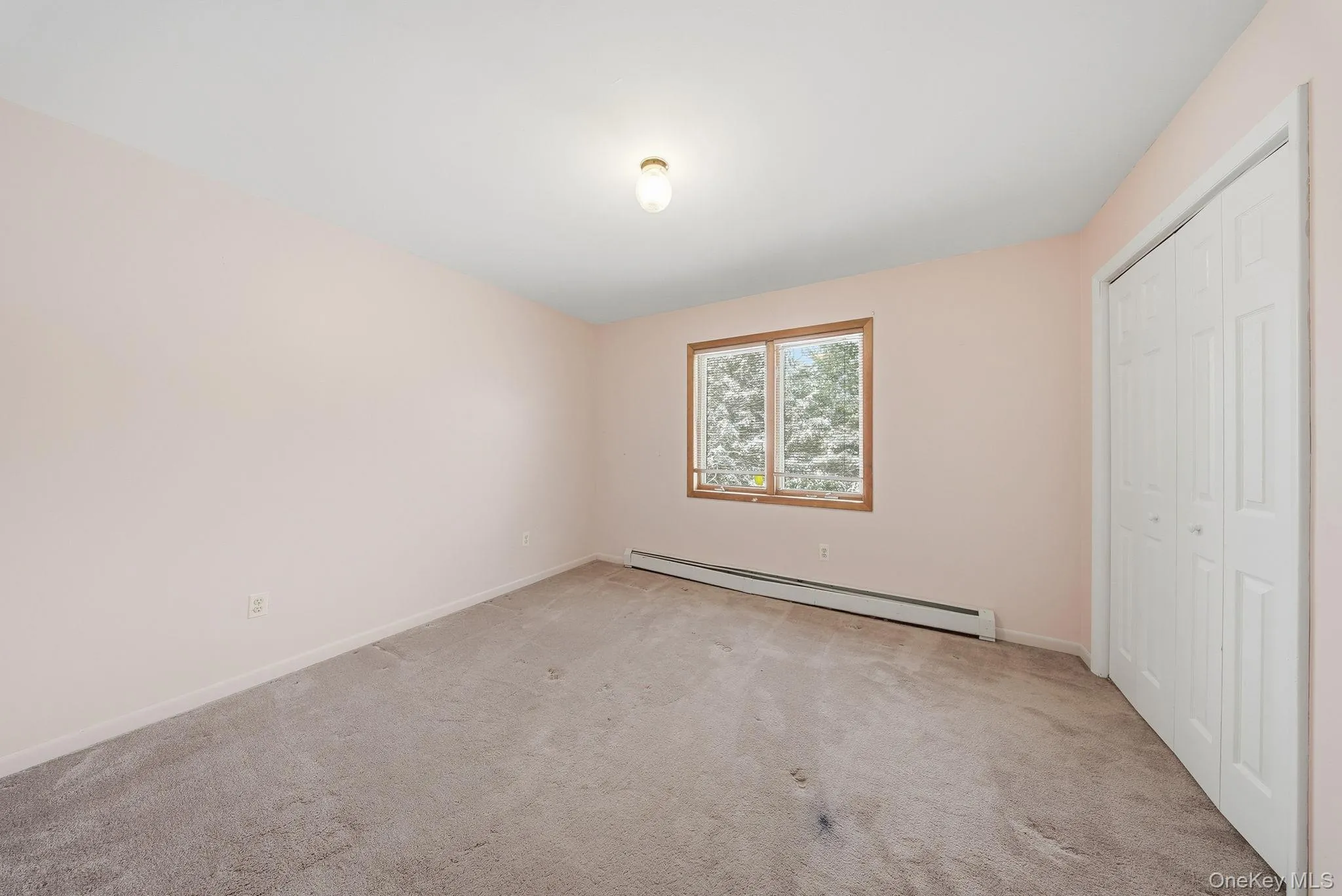 Unfurnished bedroom with a baseboard heating unit, light colored carpet, and a closet Unfurnished bedroom with a baseboard heating unit, light colored carpet, and a closet