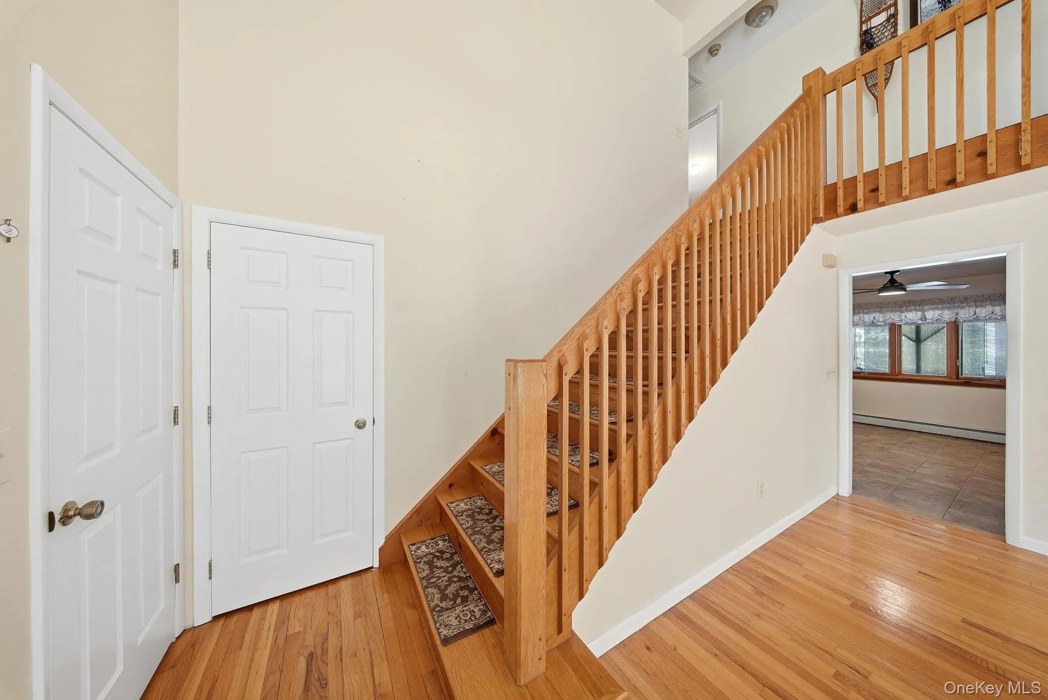 Stairway featuring a towering ceiling, wood-type flooring, a baseboard radiator, and a ceiling fan Stairway featuring a towering ceiling, wood-type flooring, a baseboard radiator, and a ceiling fan