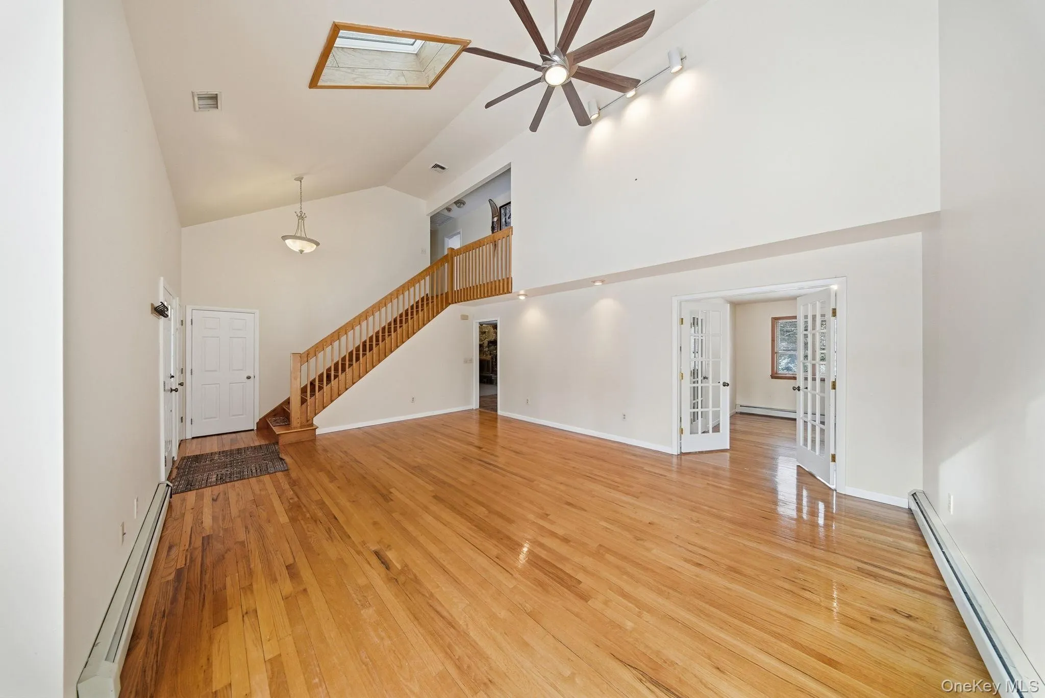 Unfurnished living room with a baseboard radiator, high vaulted ceiling, light wood-type flooring, french doors, and stairway Unfurnished living room with a baseboard radiator, high vaulted ceiling, light wood-type flooring, french doors, and stairway