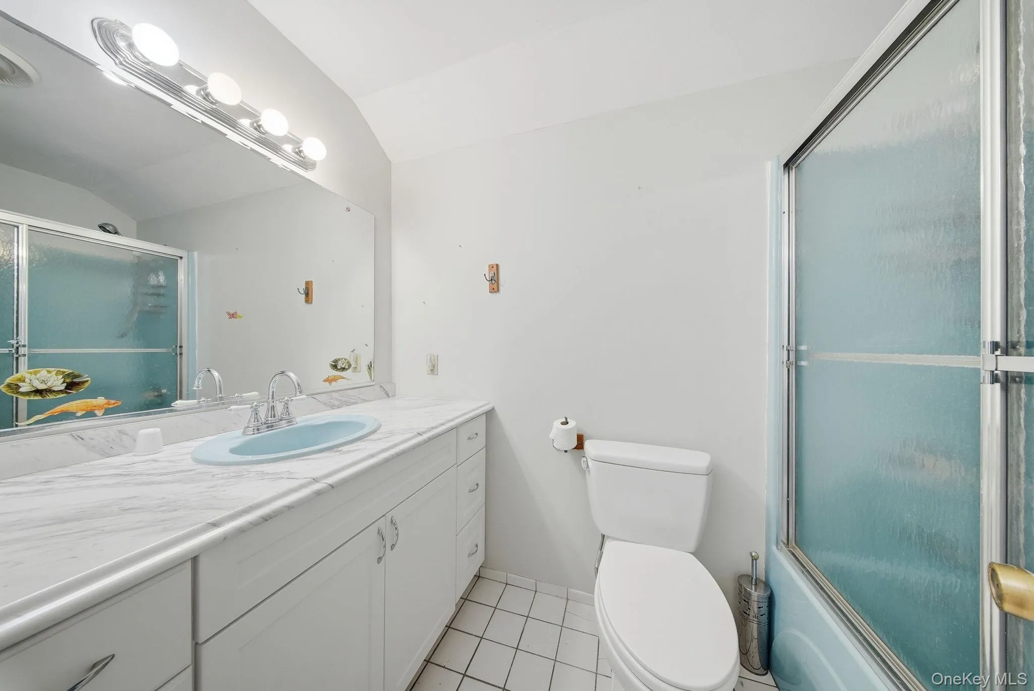 Bathroom with vanity, enclosed tub / shower combo, lofted ceiling, and light tile patterned floors Bathroom with vanity, enclosed tub / shower combo, lofted ceiling, and light tile patterned floors