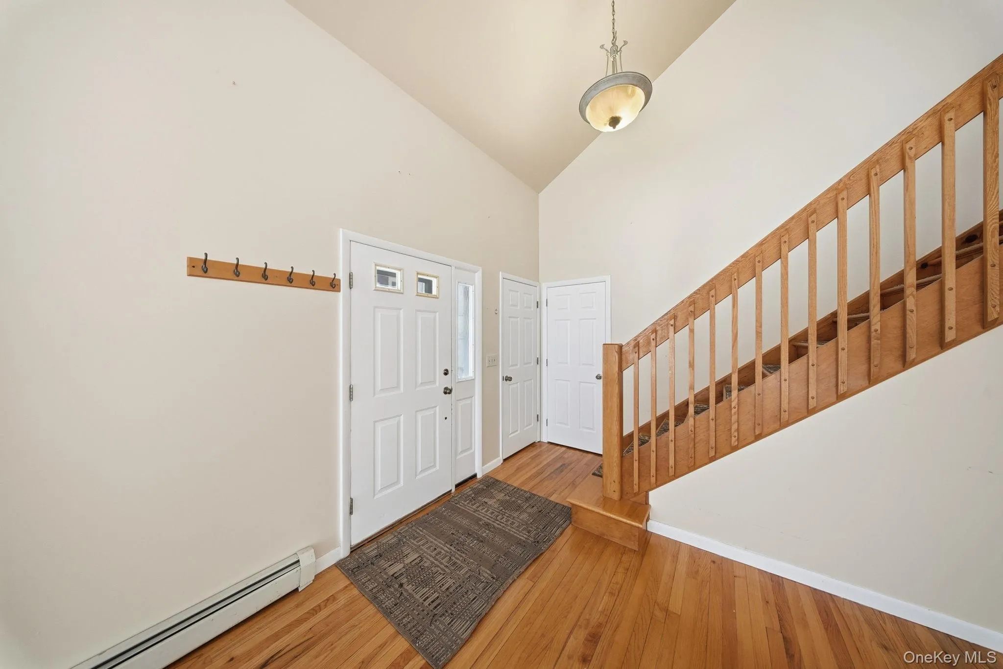 Foyer entrance with stairway, baseboard heating, high vaulted ceiling, and hardwood / wood-style floors Foyer entrance with stairway, baseboard heating, high vaulted ceiling, and hardwood / wood-style floors