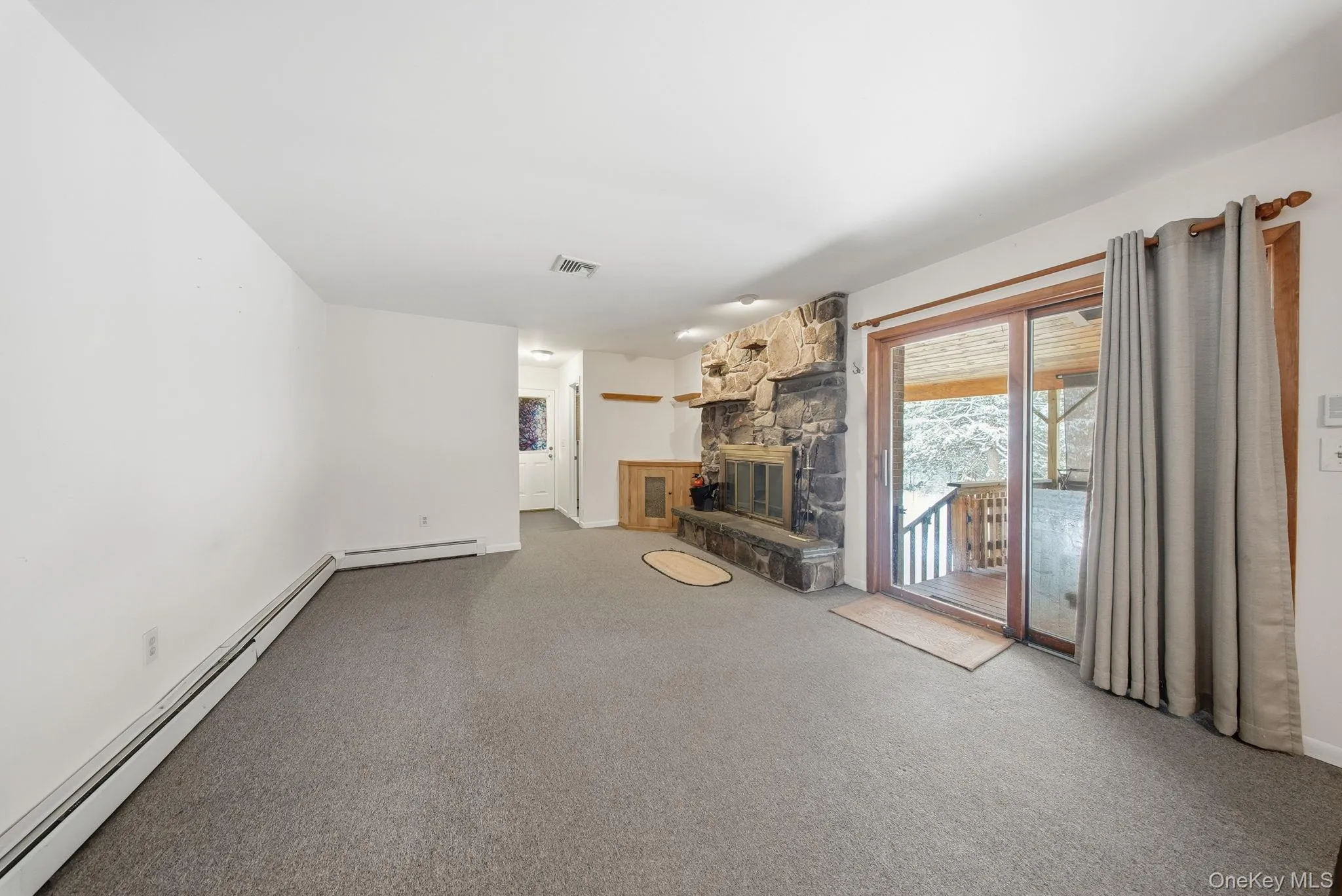 Unfurnished living room with sliders leading to a covered deck and a fireplace Unfurnished living room with sliders leading to a covered deck and a fireplace