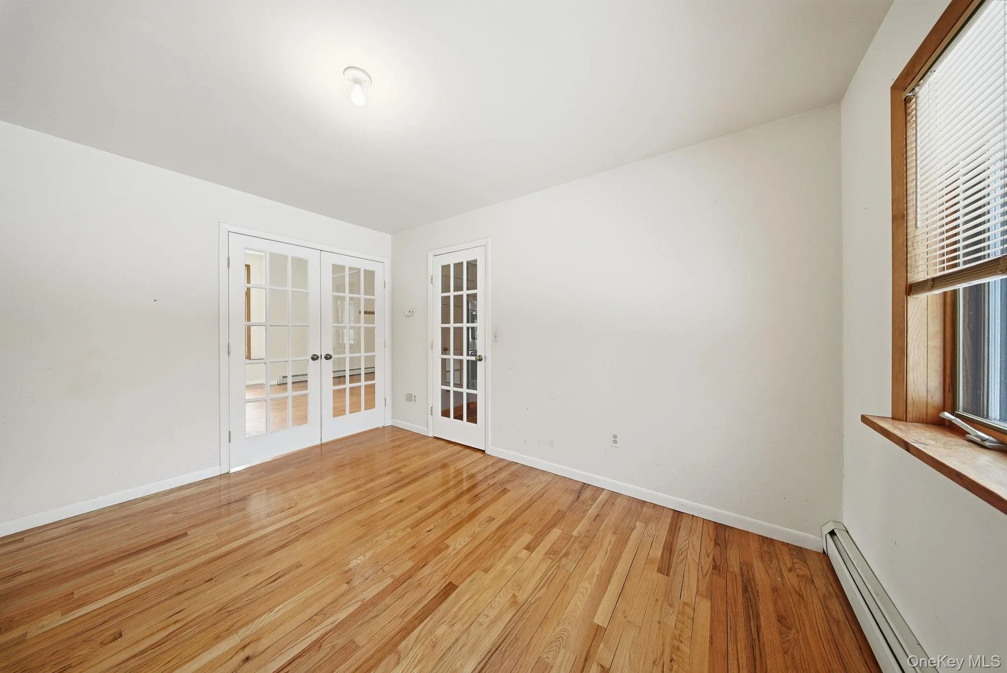 Empty room with french doors, baseboard heating, and light wood-style floors Empty room with french doors, baseboard heating, and light wood-style floors