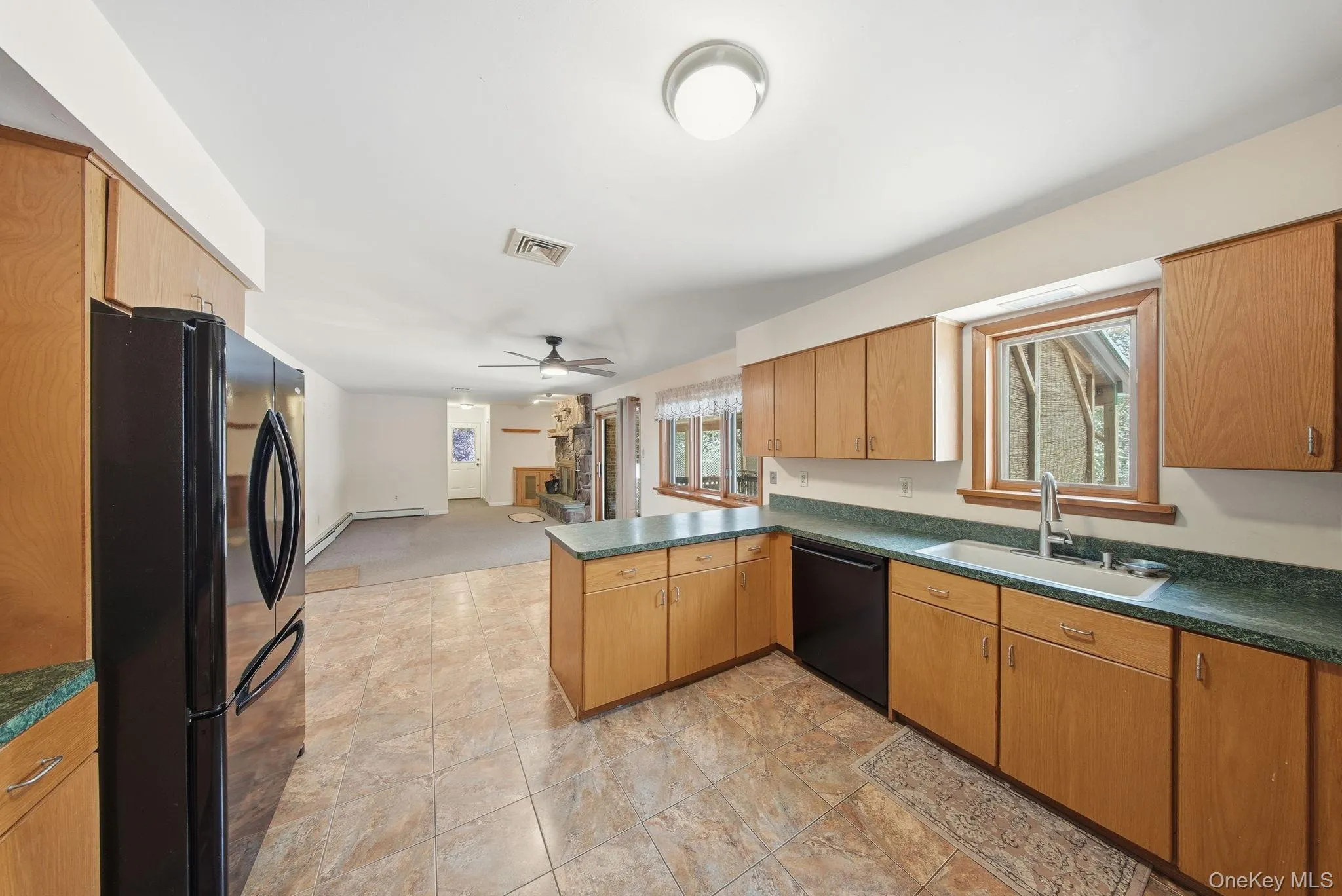 Kitchen featuring dark countertops, black appliances, a peninsula, a ceiling fan, and brown cabinets Kitchen featuring dark countertops, black appliances, a peninsula, a ceiling fan, and brown cabinets