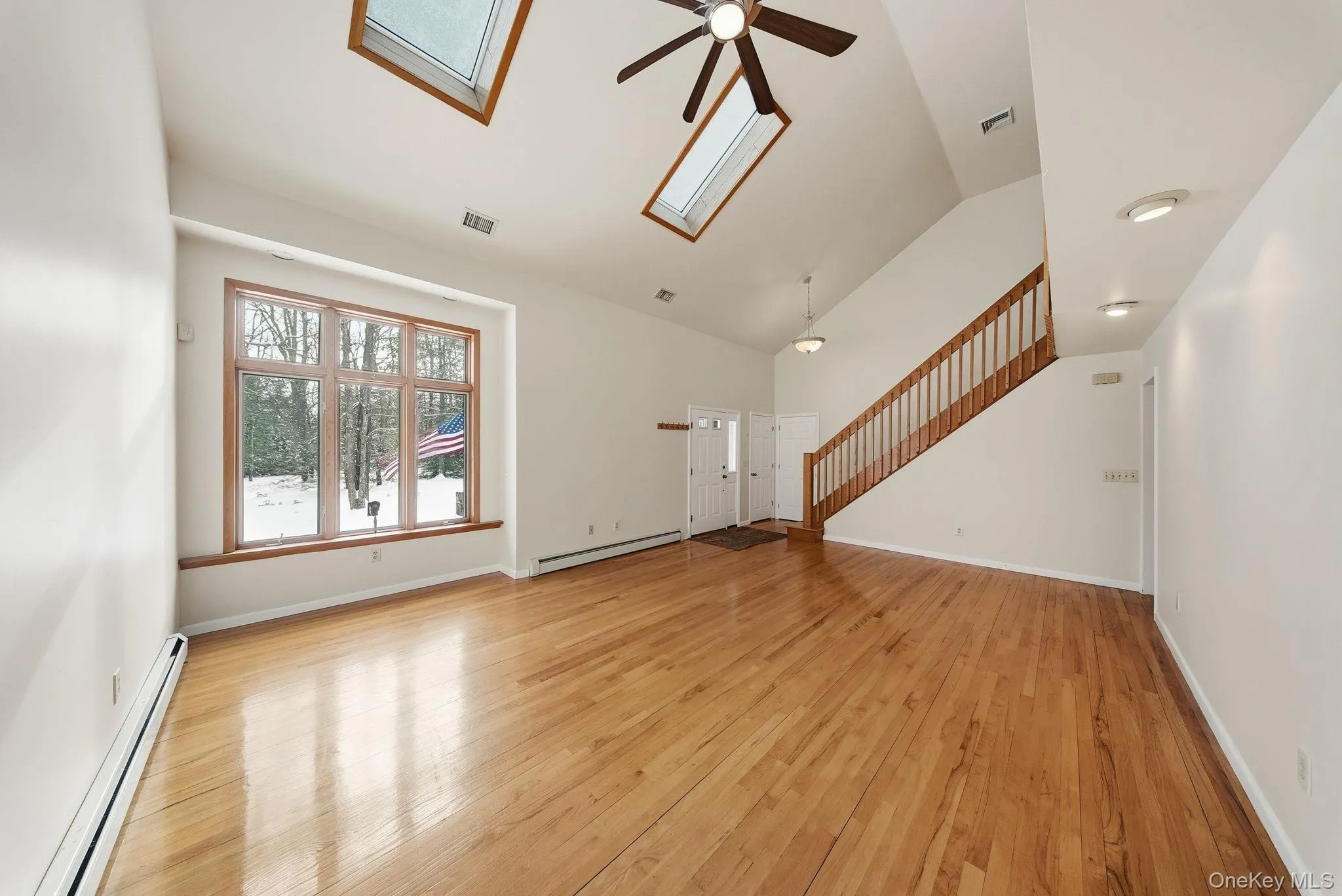 Unfurnished living room featuring baseboard heating, a skylight, light wood-type flooring, stairs, and ceiling fan Unfurnished living room featuring baseboard heating, a skylight, light wood-type flooring, stairs, and ceiling fan