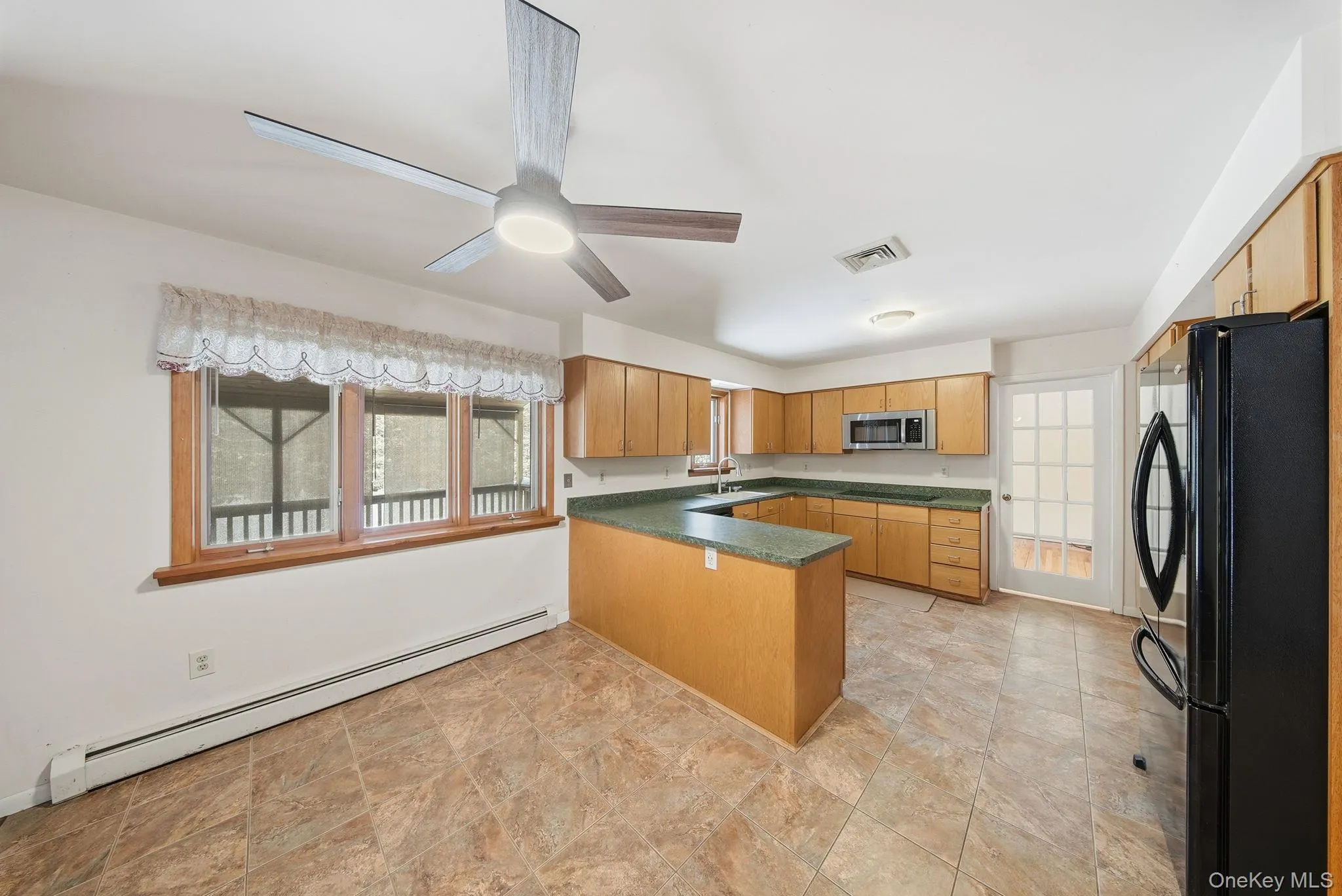 Kitchen featuring a peninsula, a baseboard heating unit, black appliances, a ceiling fan, and light brown cabinetry Kitchen featuring a peninsula, a baseboard heating unit, black appliances, a ceiling fan, and light brown cabinetry