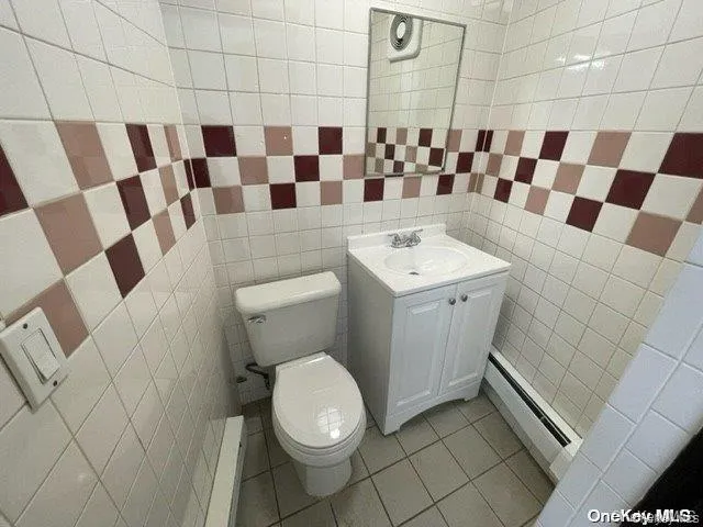 Bathroom with a baseboard radiator, vanity, tile patterned floors, and tile walls Bathroom with a baseboard radiator, vanity, tile patterned floors, and tile walls