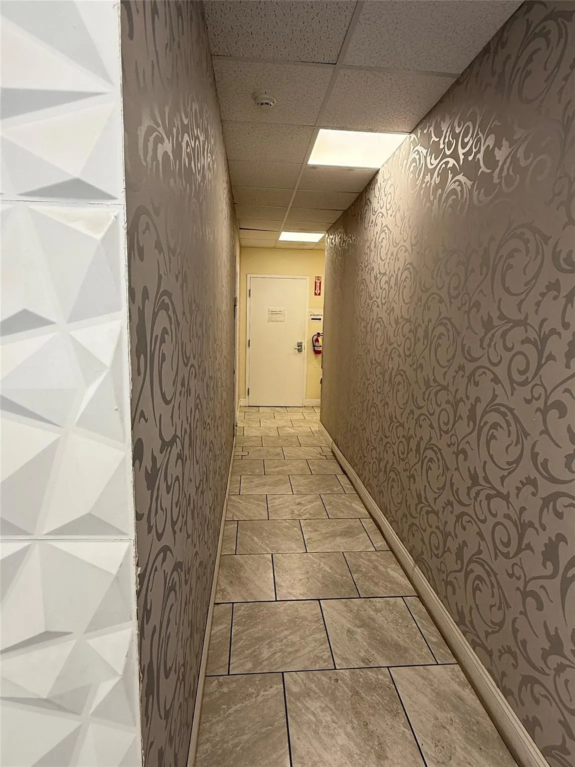 Hallway with wallpapered walls and a paneled ceiling Hallway with wallpapered walls and a paneled ceiling