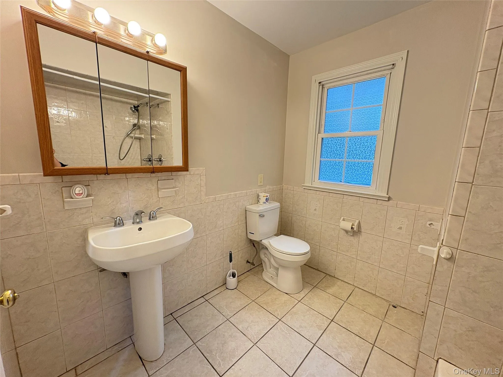 Bathroom featuring tile walls, wainscoting, tile patterned flooring, and a shower Bathroom featuring tile walls, wainscoting, tile patterned flooring, and a shower