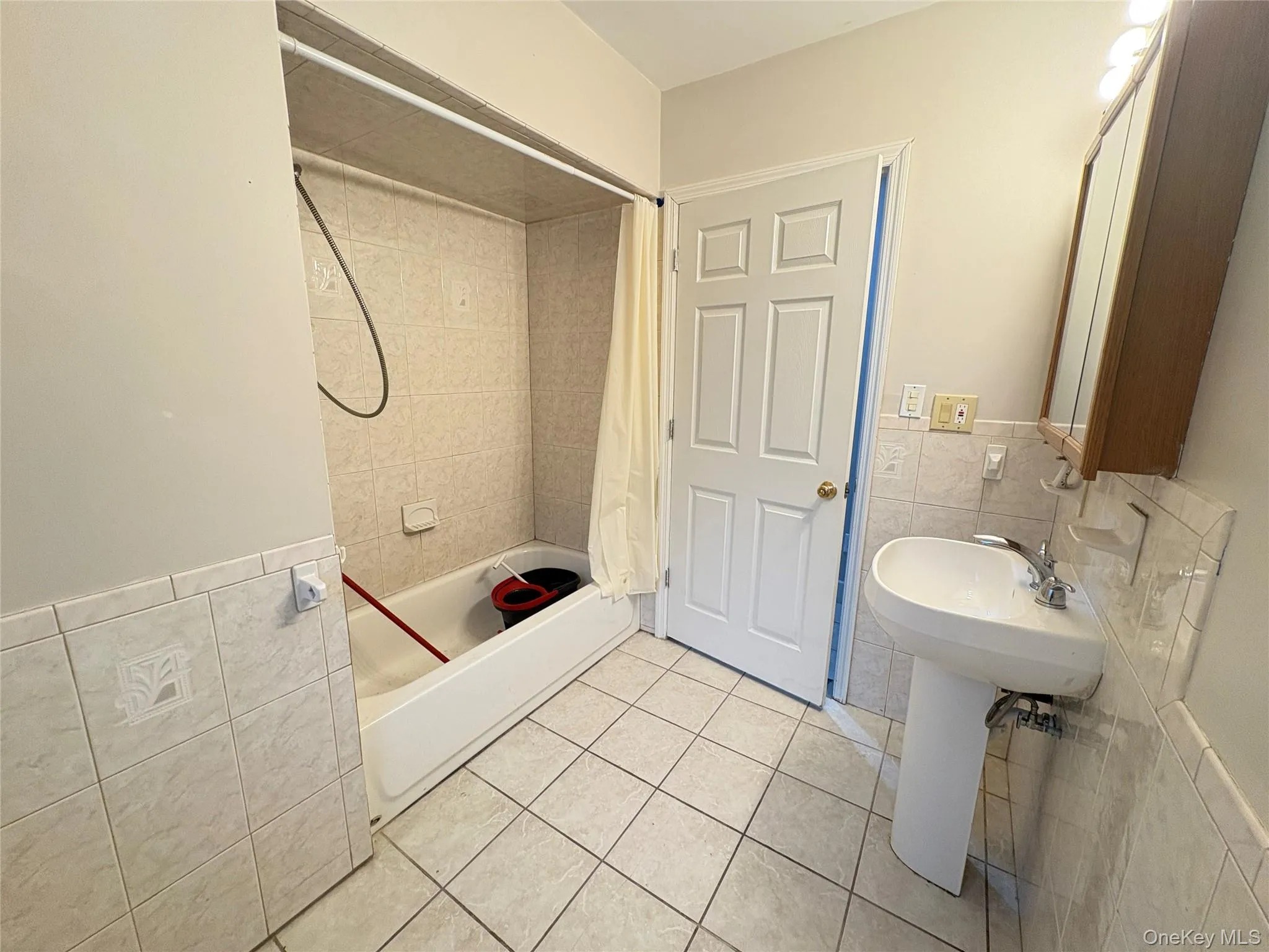 Full bathroom featuring tile walls, tile patterned flooring, shower / bathtub combination with curtain, and wainscoting Full bathroom featuring tile walls, tile patterned flooring, shower / bathtub combination with curtain, and wainscoting