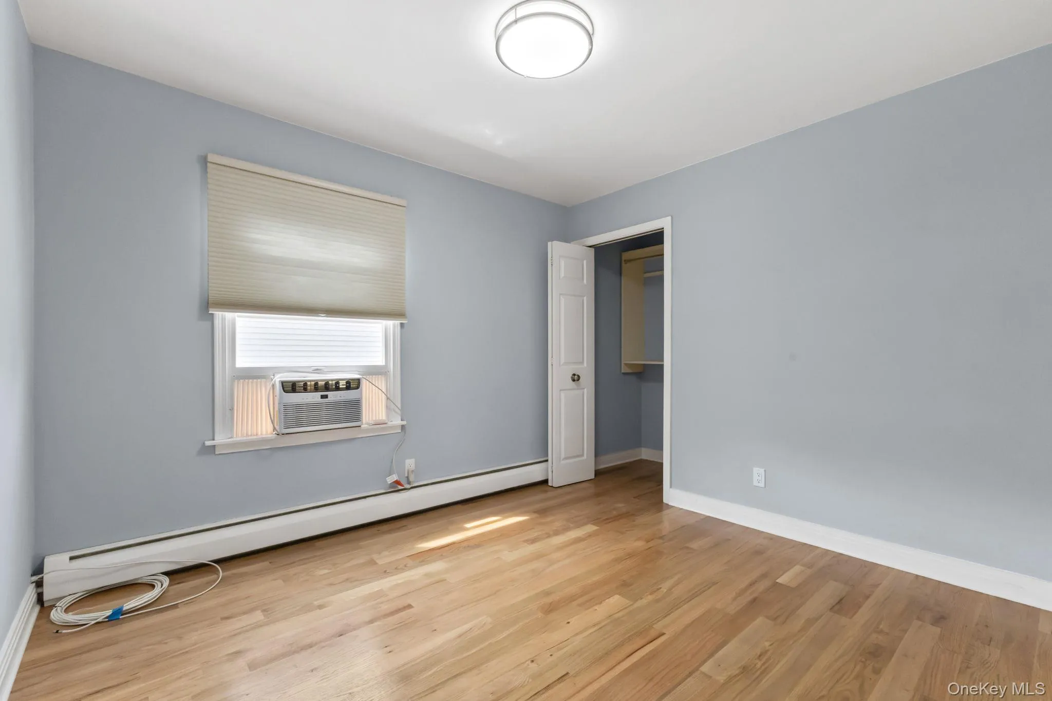 Unfurnished bedroom with a baseboard heating unit, a walk in closet, light wood-style floors, and cooling unit Unfurnished bedroom with a baseboard heating unit, a walk in closet, light wood-style floors, and cooling unit