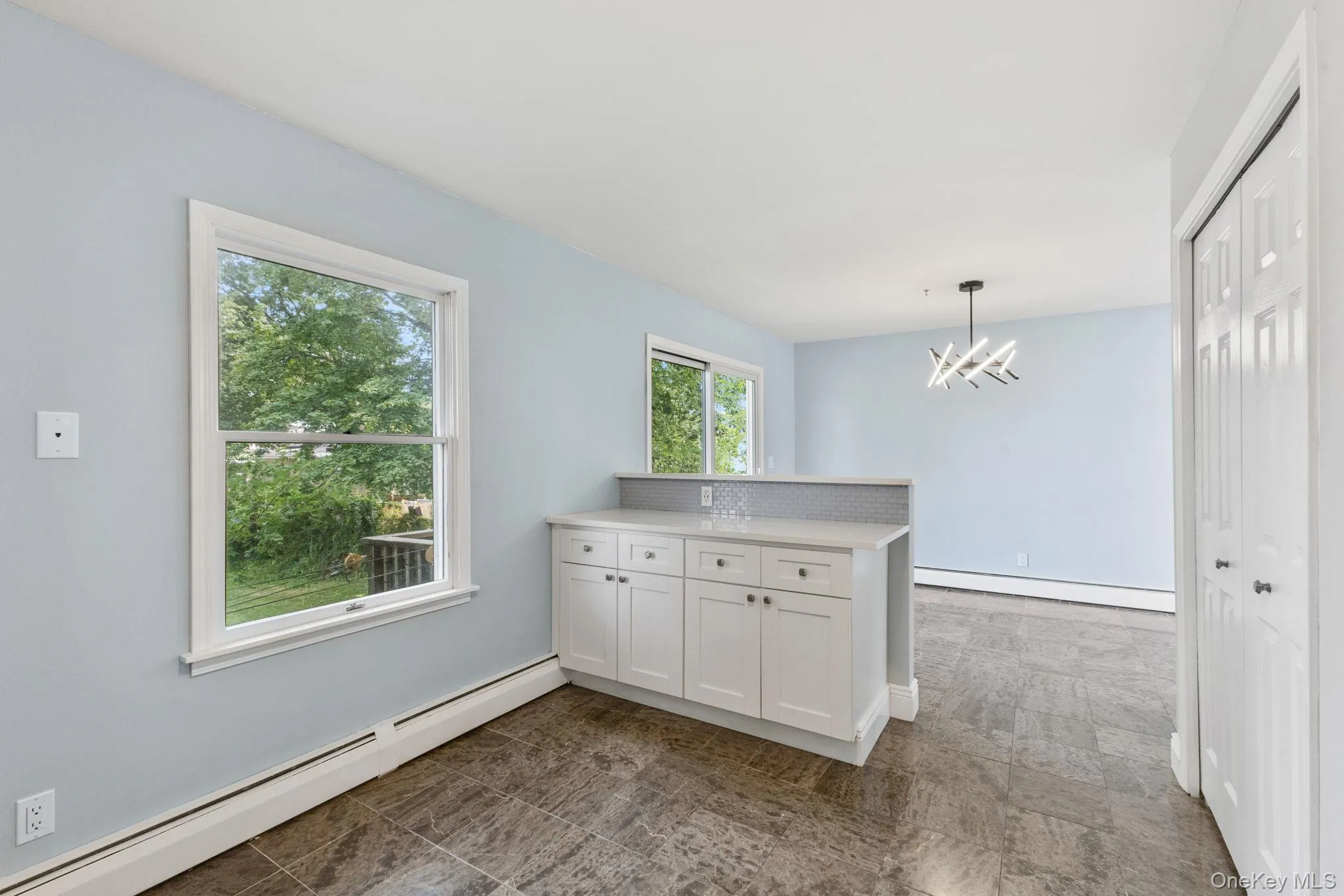 Kitchen with a baseboard heating unit, white cabinets, a peninsula, and decorative light fixtures Kitchen with a baseboard heating unit, white cabinets, a peninsula, and decorative light fixtures
