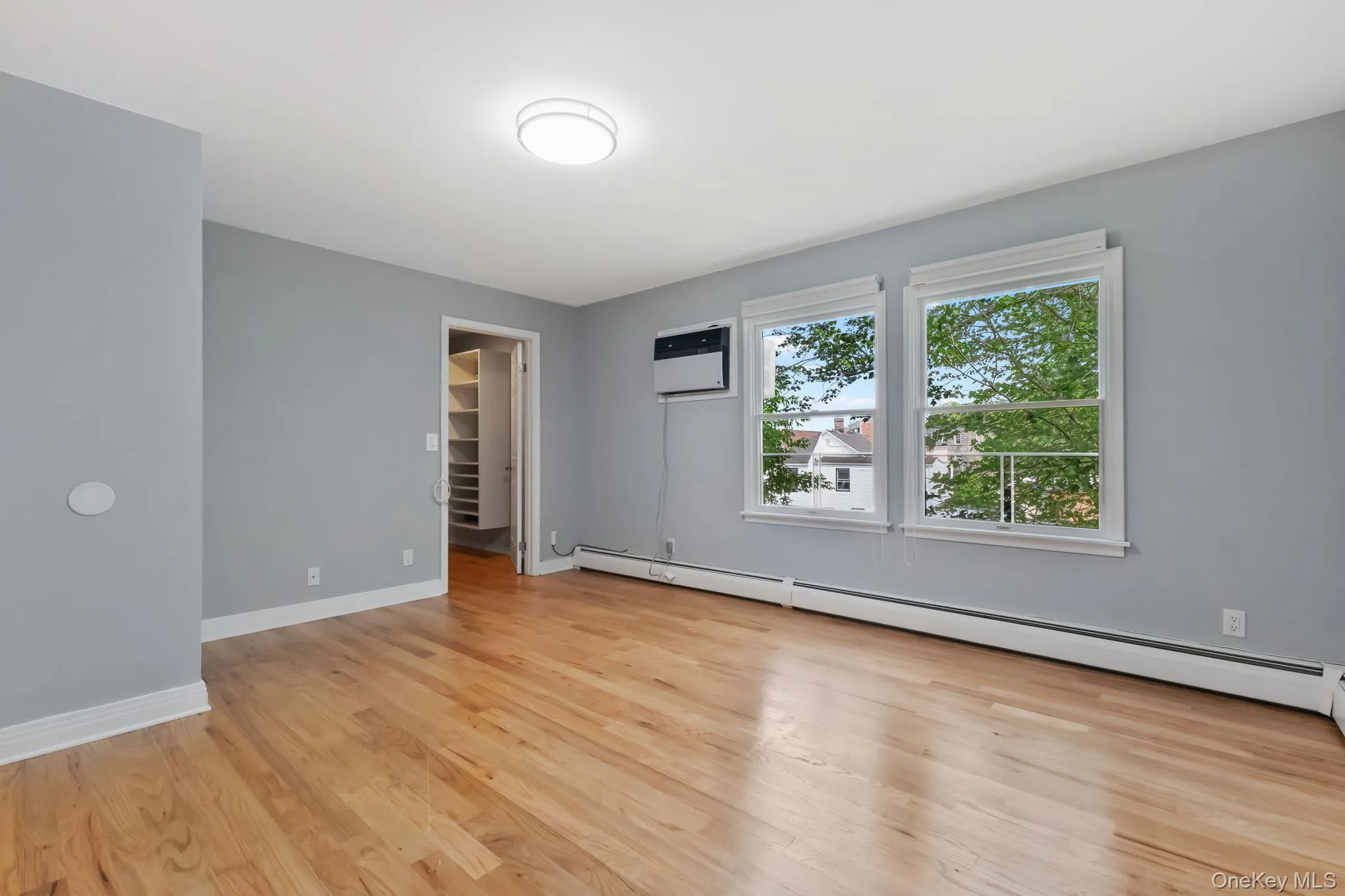 Unfurnished bedroom with a walk in closet, a baseboard radiator, light wood finished floors, and a wall mounted AC Unfurnished bedroom with a walk in closet, a baseboard radiator, light wood finished floors, and a wall mounted AC