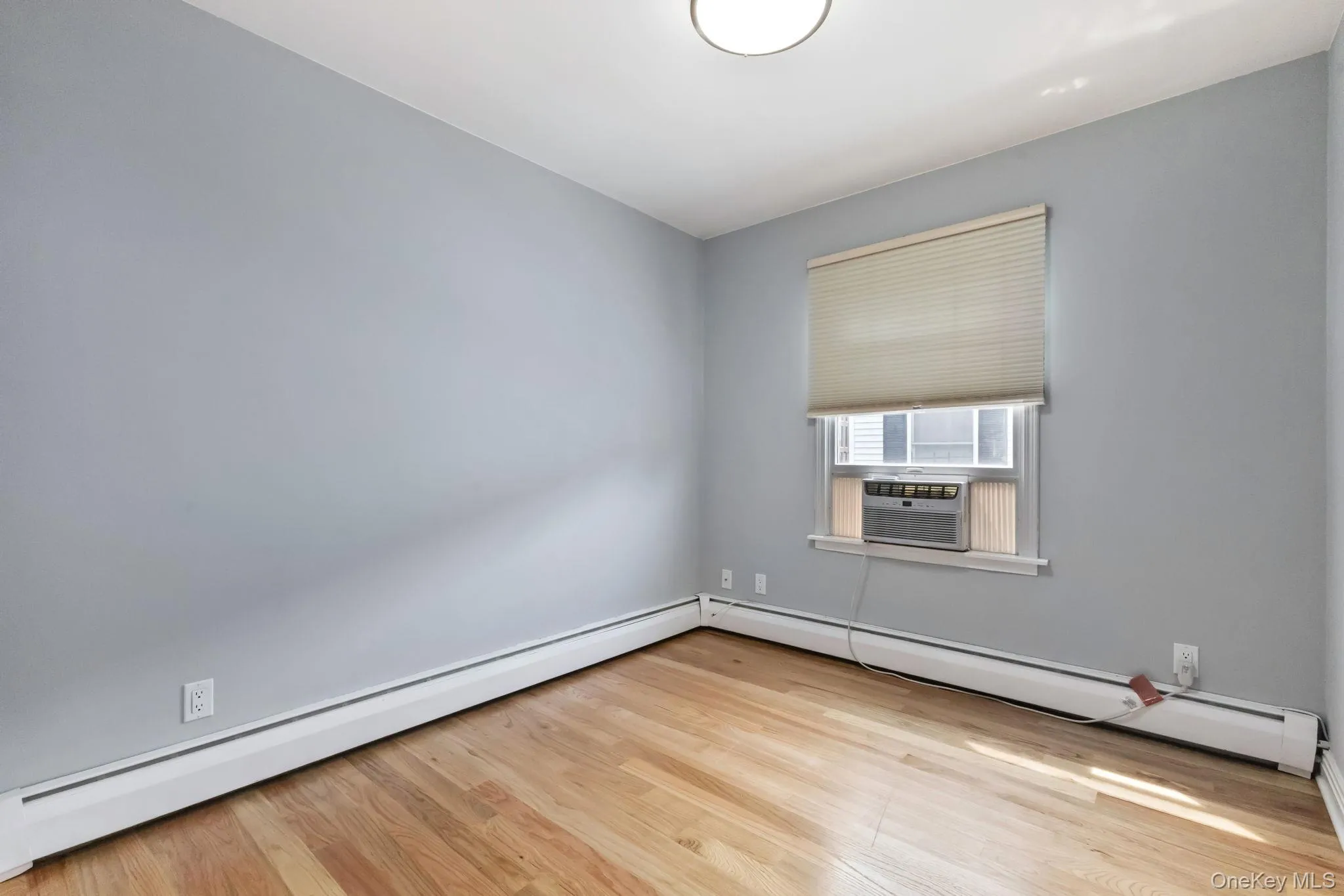 Unfurnished room featuring baseboard heating, light wood-style flooring, a baseboard heating unit, and cooling unit Unfurnished room featuring baseboard heating, light wood-style flooring, a baseboard heating unit, and cooling unit
