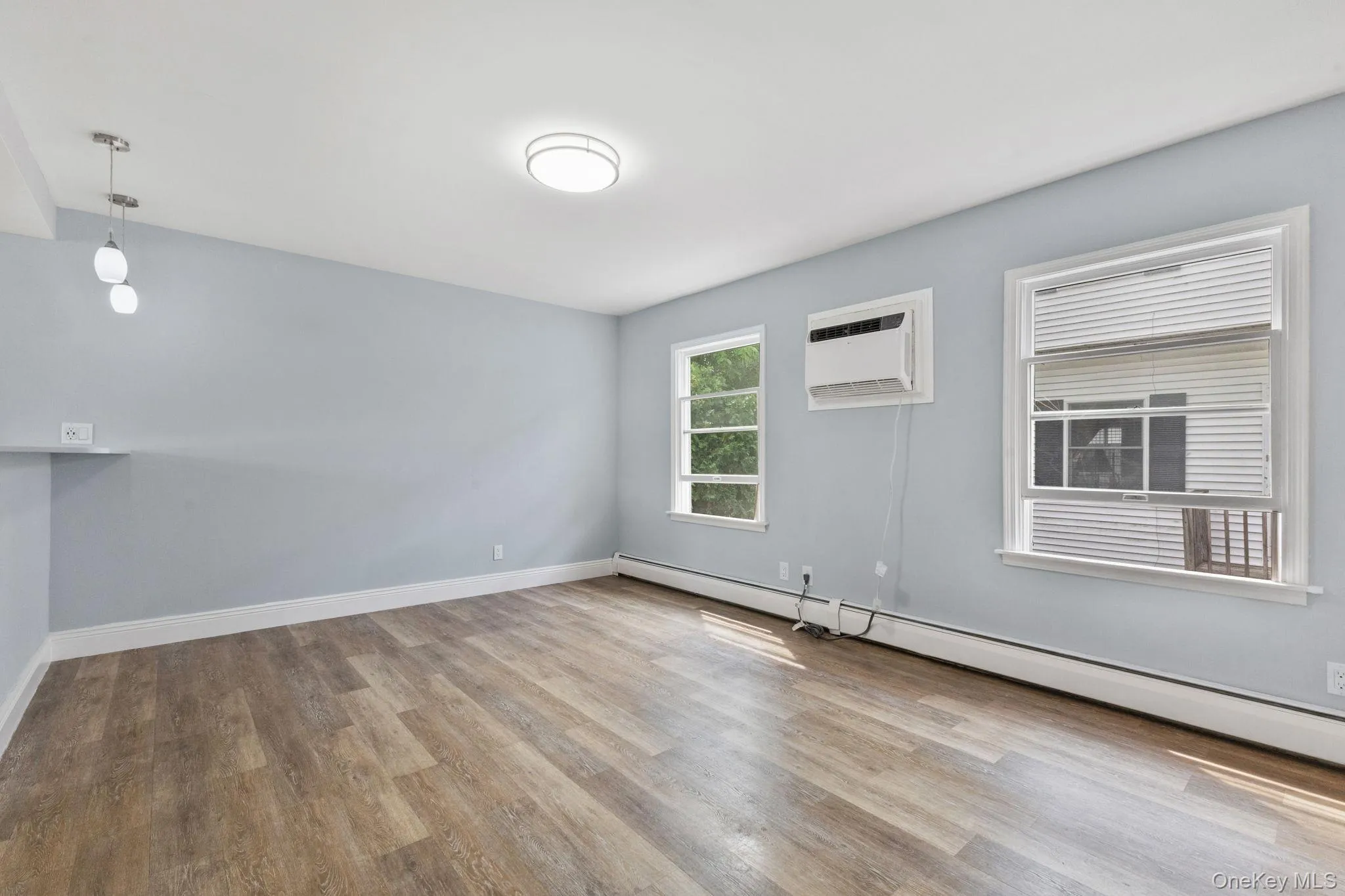 Unfurnished room featuring a baseboard radiator, light wood-style floors, and a wall unit AC Unfurnished room featuring a baseboard radiator, light wood-style floors, and a wall unit AC
