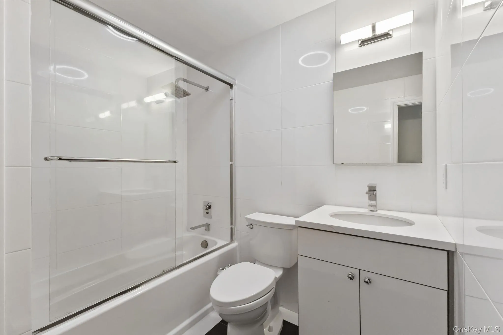 Full bathroom featuring combined bath / shower with glass door, vanity, and tile walls Full bathroom featuring combined bath / shower with glass door, vanity, and tile walls
