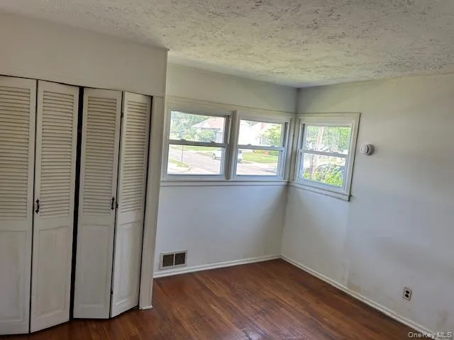 Unfurnished bedroom featuring dark wood-type flooring, a closet, and a textured ceiling Unfurnished bedroom featuring dark wood-type flooring, a closet, and a textured ceiling