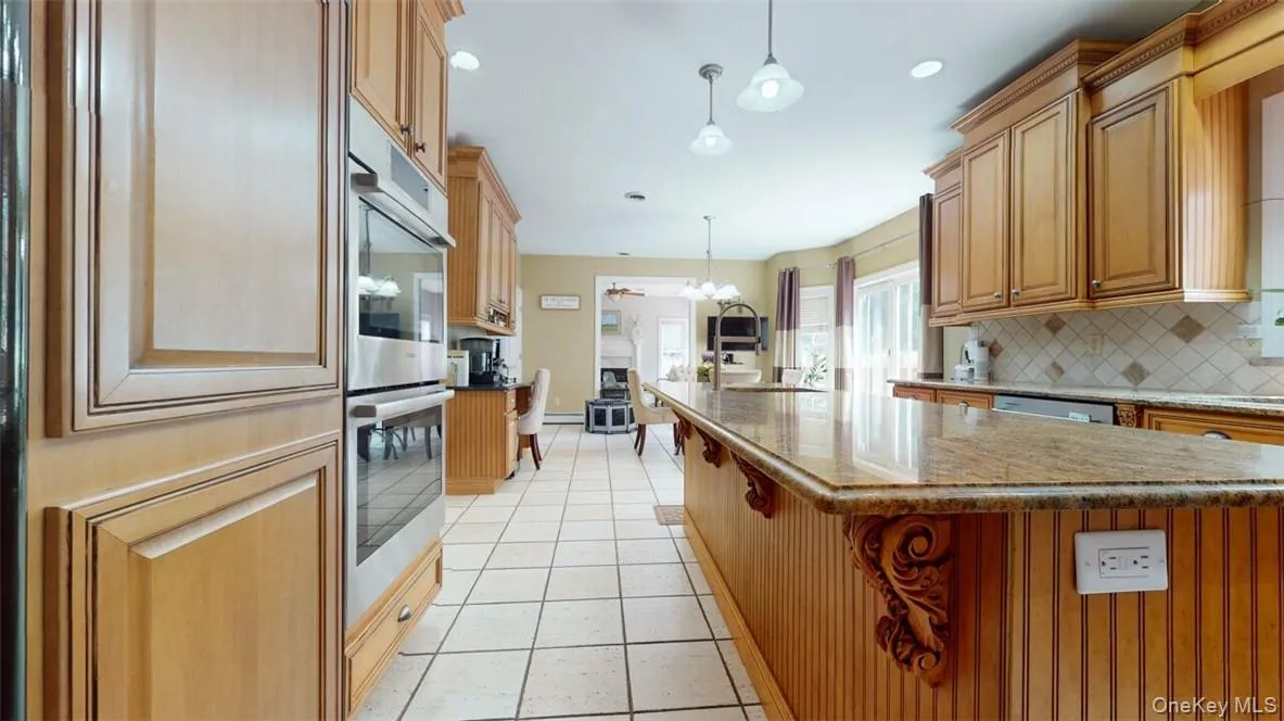Kitchen featuring a kitchen island with sink, backsplash, hanging light fixtures, and stainless steel appliances Kitchen featuring a kitchen island with sink, backsplash, hanging light fixtures, and stainless steel appliances