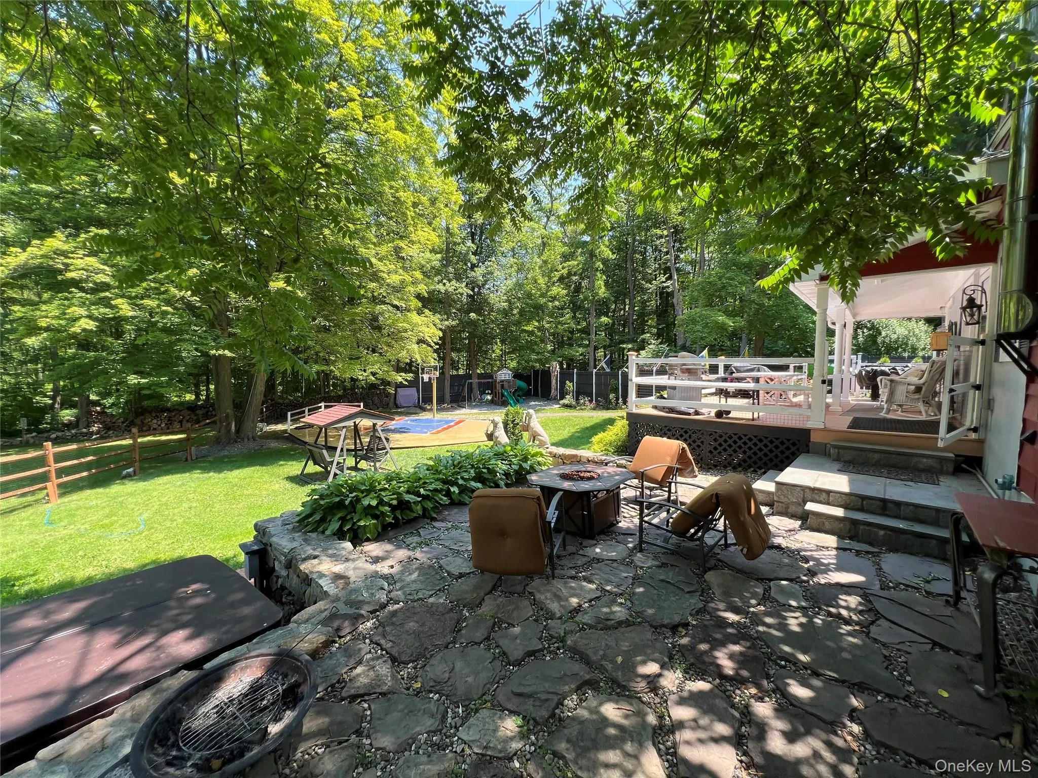 View of patio featuring a fire pit, a wooden deck, and view of wooded area View of patio featuring a fire pit, a wooden deck, and view of wooded area