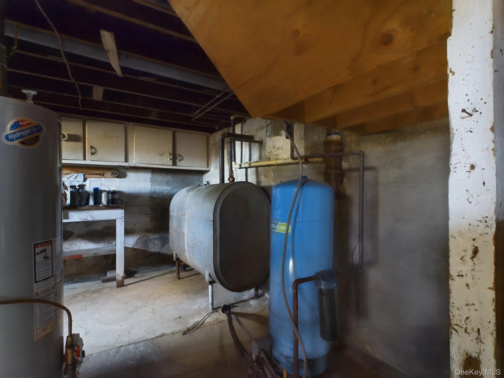 Unfinished below grade area with water heater, oil tank, and a water pressure tank Unfinished below grade area with water heater, oil tank, and a water pressure tank