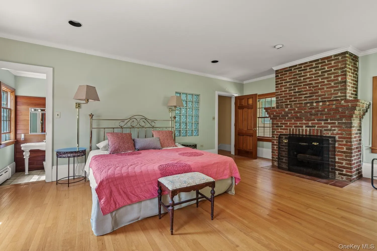 Bedroom with ornamental molding, light wood finished floors, a brick fireplace, and connected bathroom Bedroom with ornamental molding, light wood finished floors, a brick fireplace, and connected bathroom