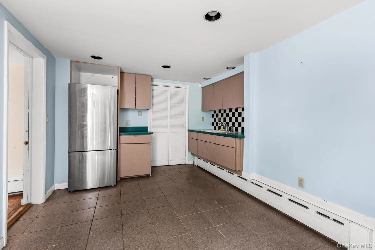 Lower level summer kitchen featuring cast iron baseboard heating, light brown cabinets, freestanding refrigerator, tasteful backsplash, and dark countertops Lower level summer kitchen featuring cast iron baseboard heating, light brown cabinets, freestanding refrigerator, tasteful backsplash, and dark countertops