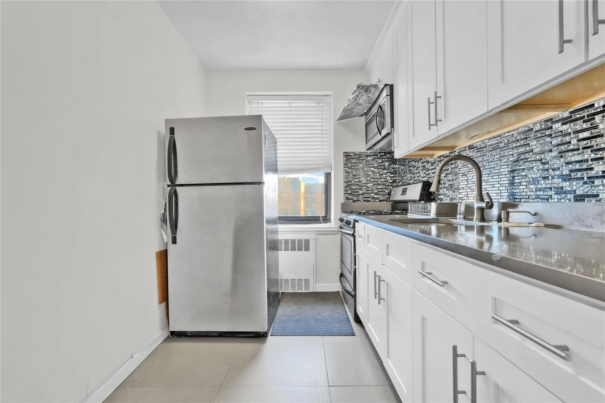 Kitchen with appliances with stainless steel finishes, radiator, tasteful backsplash, white cabinets, and dark countertops Kitchen with appliances with stainless steel finishes, radiator, tasteful backsplash, white cabinets, and dark countertops