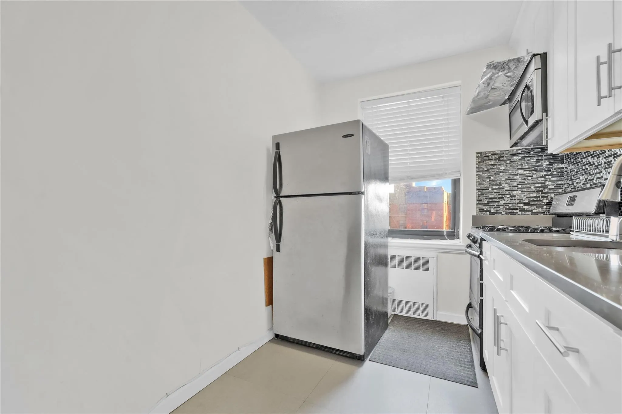 Kitchen featuring appliances with stainless steel finishes, radiator, decorative backsplash, and white cabinetry Kitchen featuring appliances with stainless steel finishes, radiator, decorative backsplash, and white cabinetry