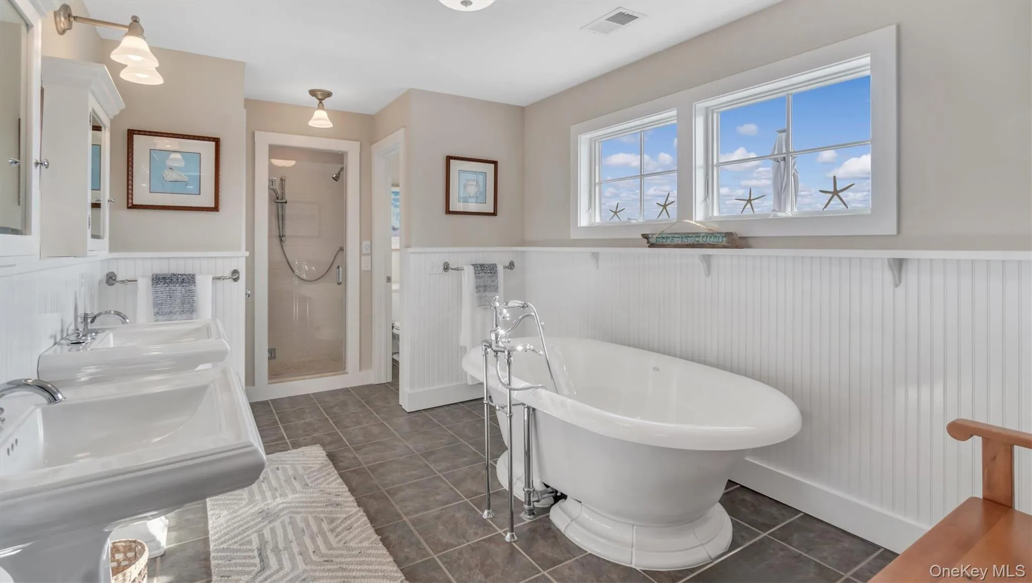 Bathroom featuring wainscoting, a shower stall, a freestanding bath, tile patterned floors, and double vanity Bathroom featuring wainscoting, a shower stall, a freestanding bath, tile patterned floors, and double vanity