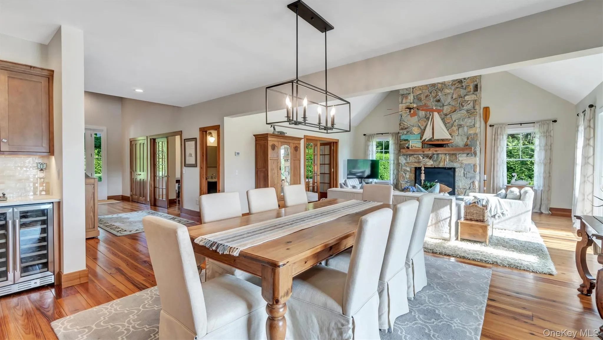 Dining space featuring beverage cooler, lofted ceiling, light wood-style flooring, a stone fireplace, and a dry bar Dining space featuring beverage cooler, lofted ceiling, light wood-style flooring, a stone fireplace, and a dry bar